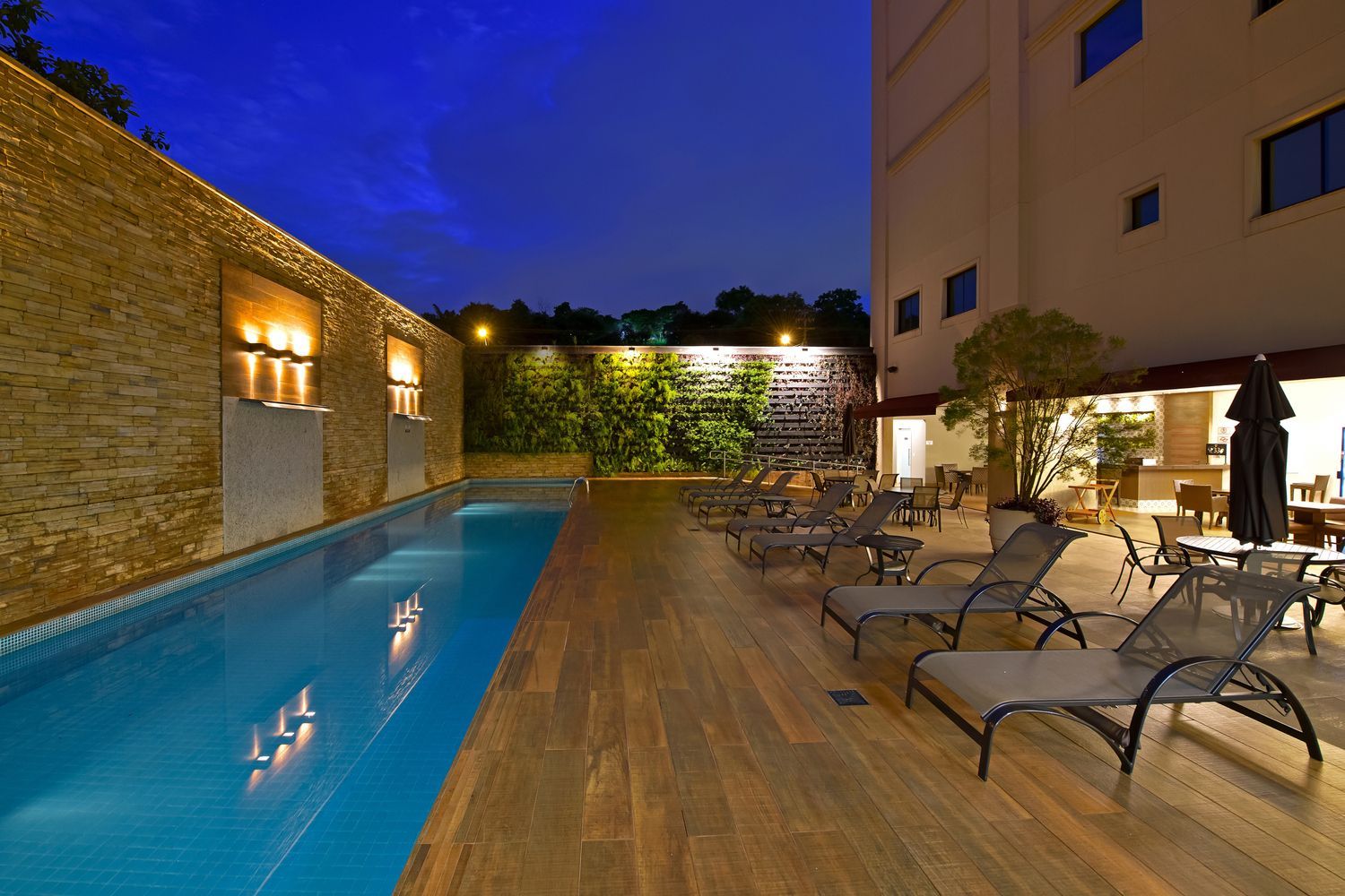 Uma grande piscina é cercada por cadeiras e mesas à noite.