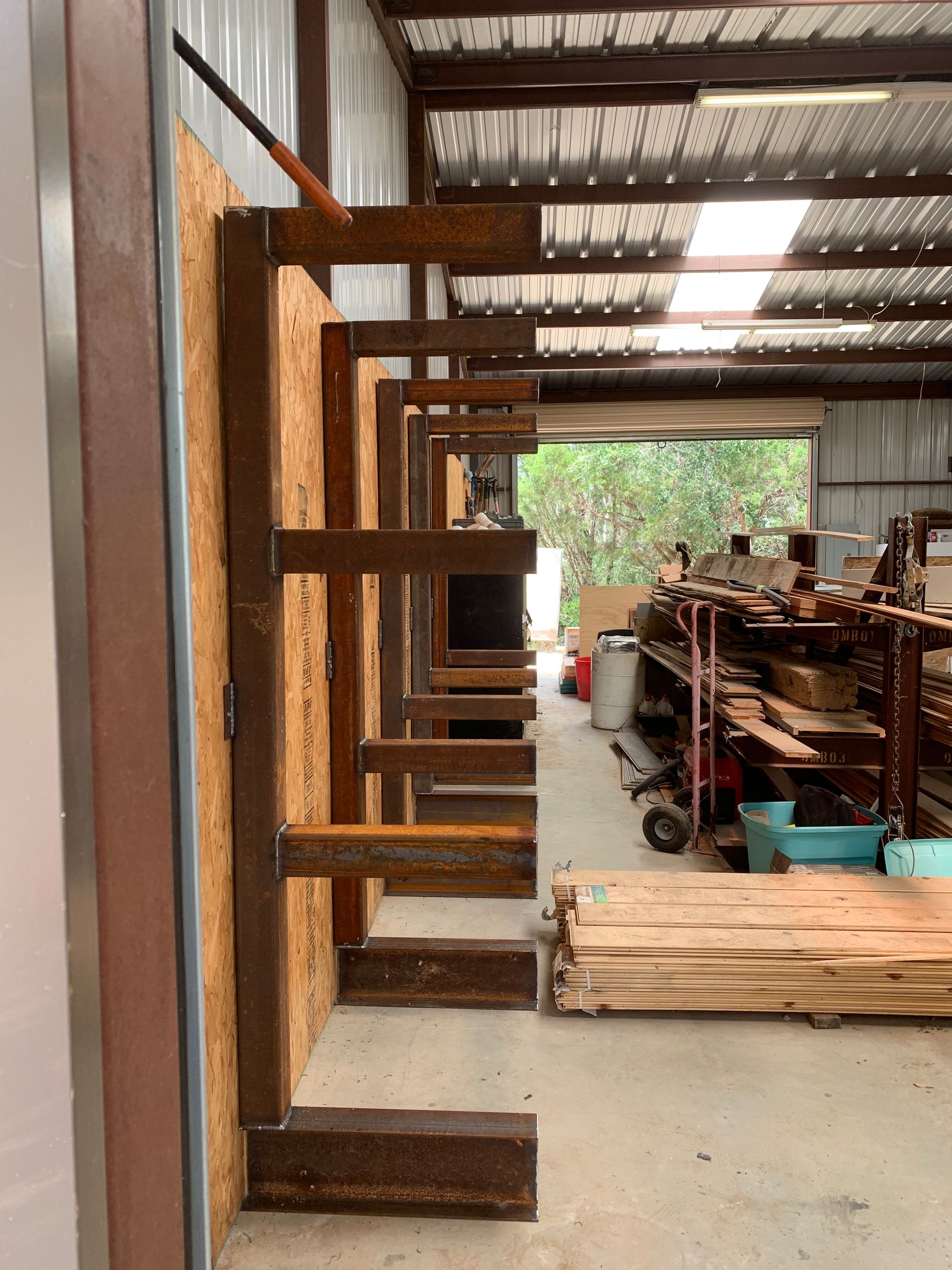 Rusty metal frame structure in a workshop, with shelves, tools, and wood stacked inside.