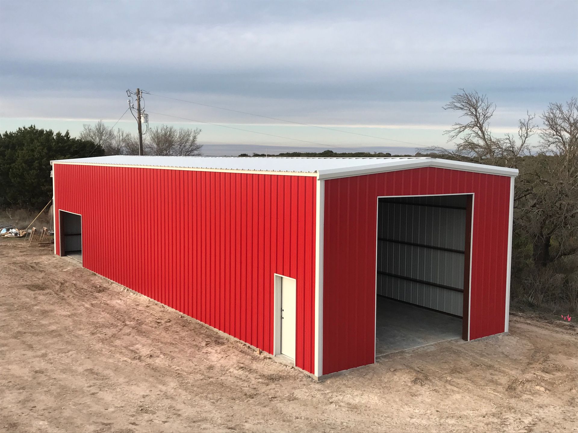 Red metal storage shed with open front and white trim in a rural dirt lot