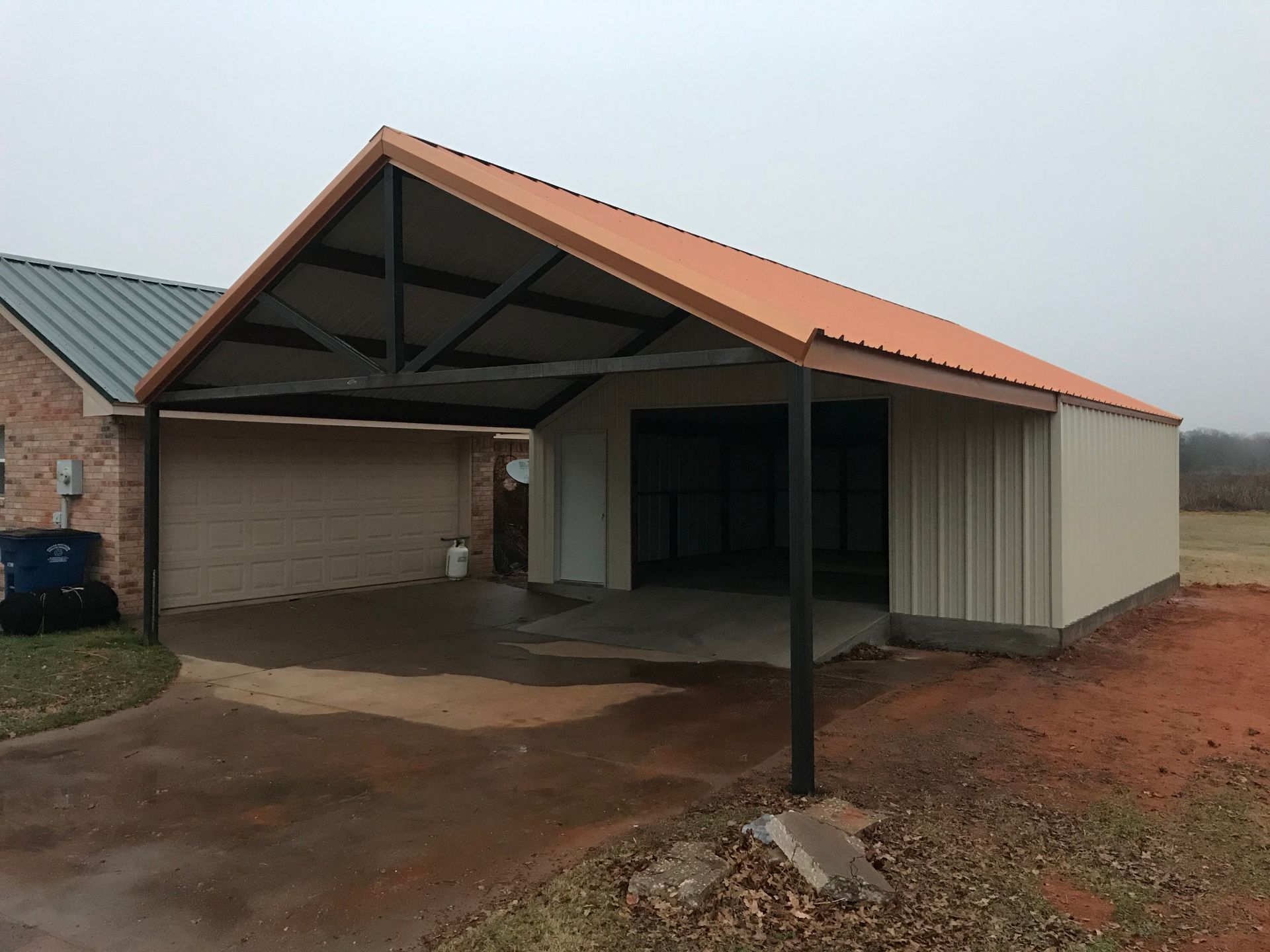 Covered carport with a corrugated metal roof and brick support posts on a concrete driveway