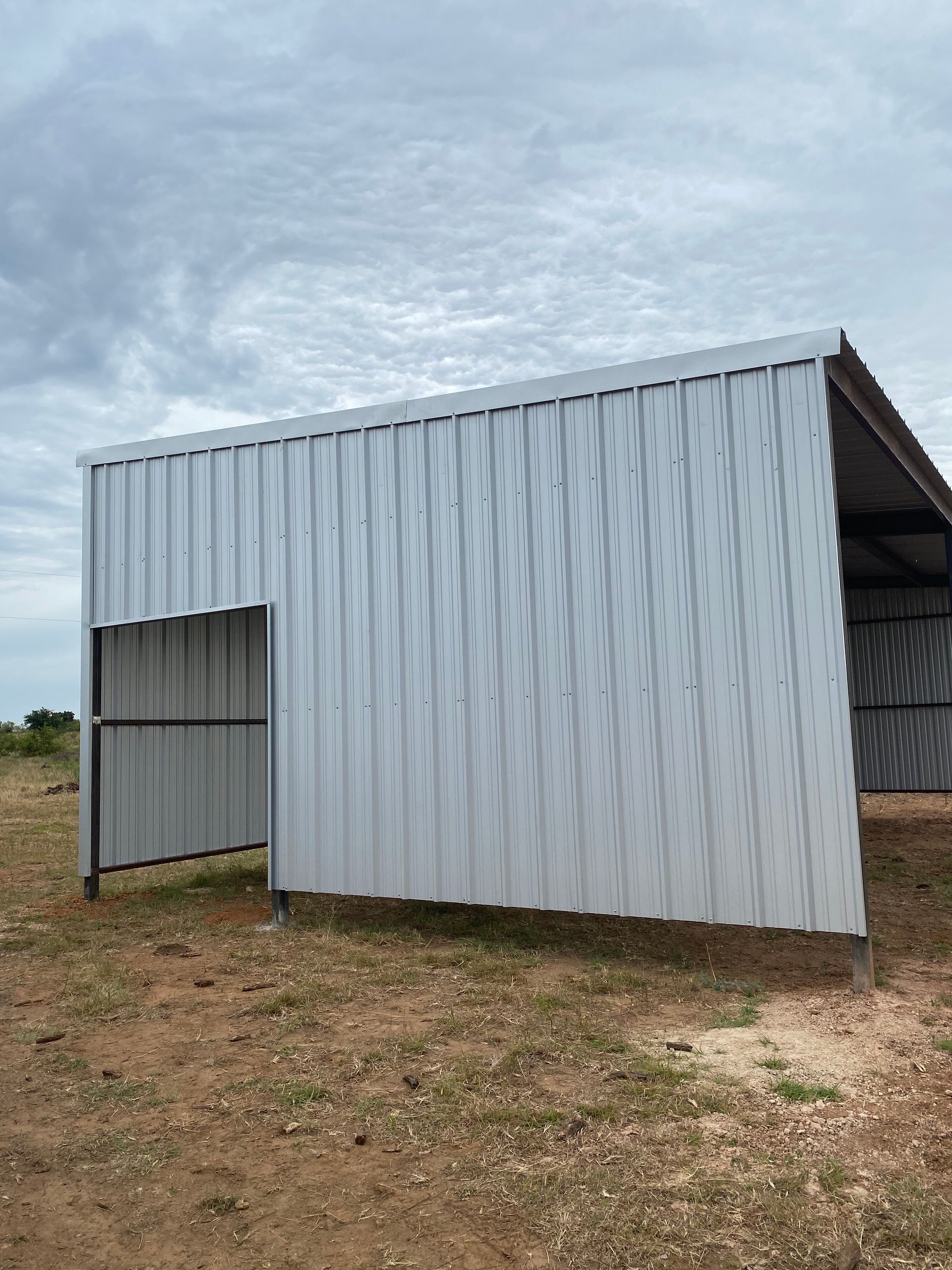 Small corrugated metal shed on bare ground under a cloudy sky
