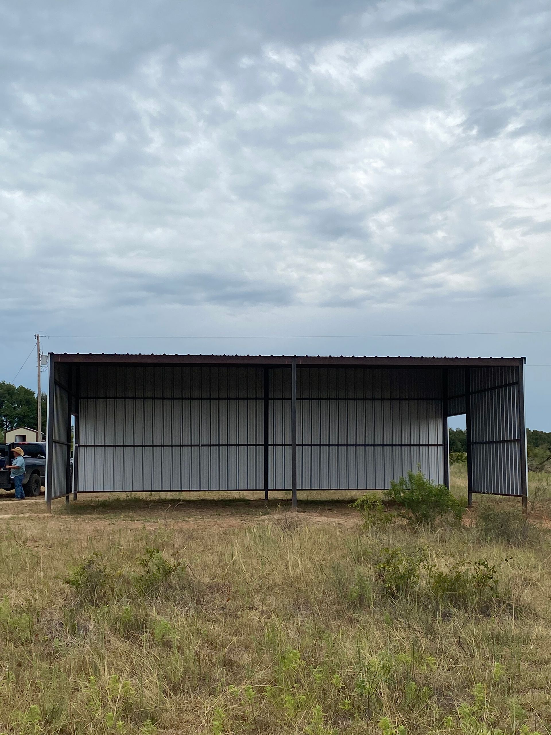 Small corrugated metal shed in a grassy field under a cloudy sky