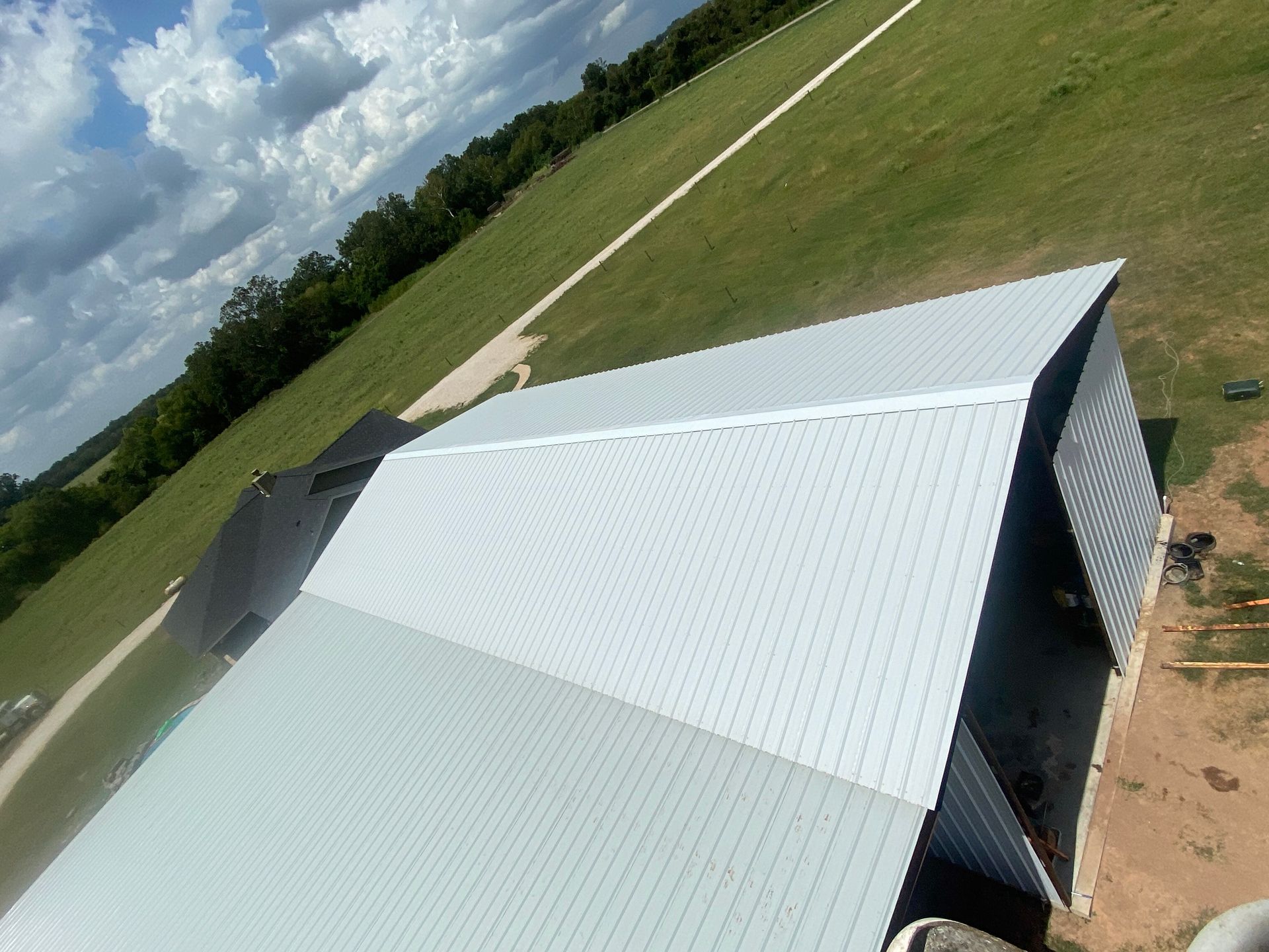 Tilted white metal-roof building in a grassy rural field under a partly cloudy sky