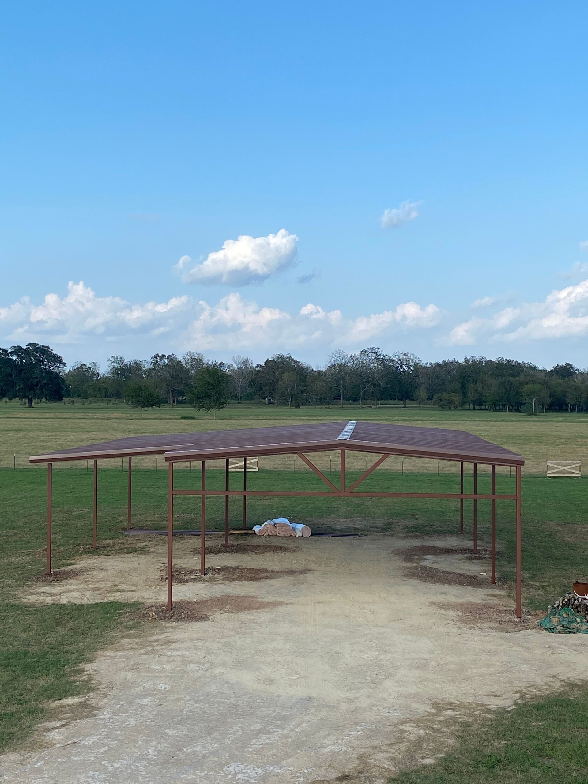 Simple rural shelter with a rusty metal roof on a dirt path, under a blue sky with clouds.
