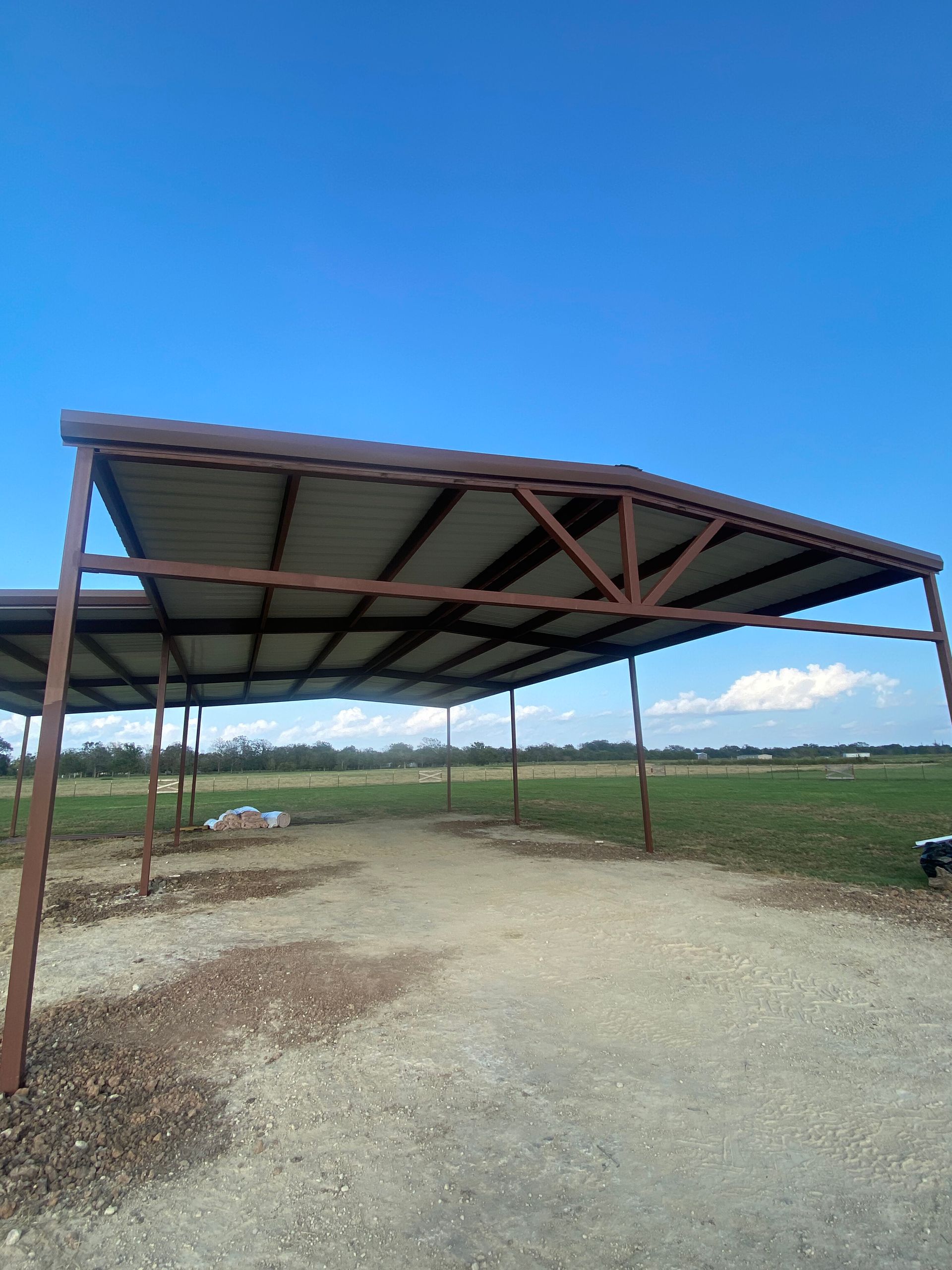 Open metal shed in a gravel lot under a clear blue sky, overlooking open fields.