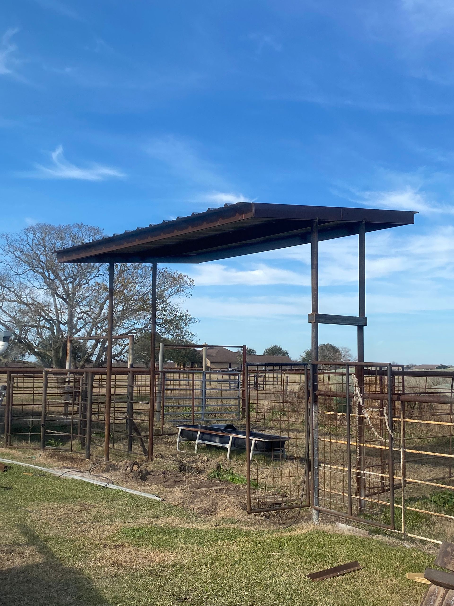 Open-sided farm shelter with corrugated metal roof in a fenced pasture under a blue sky