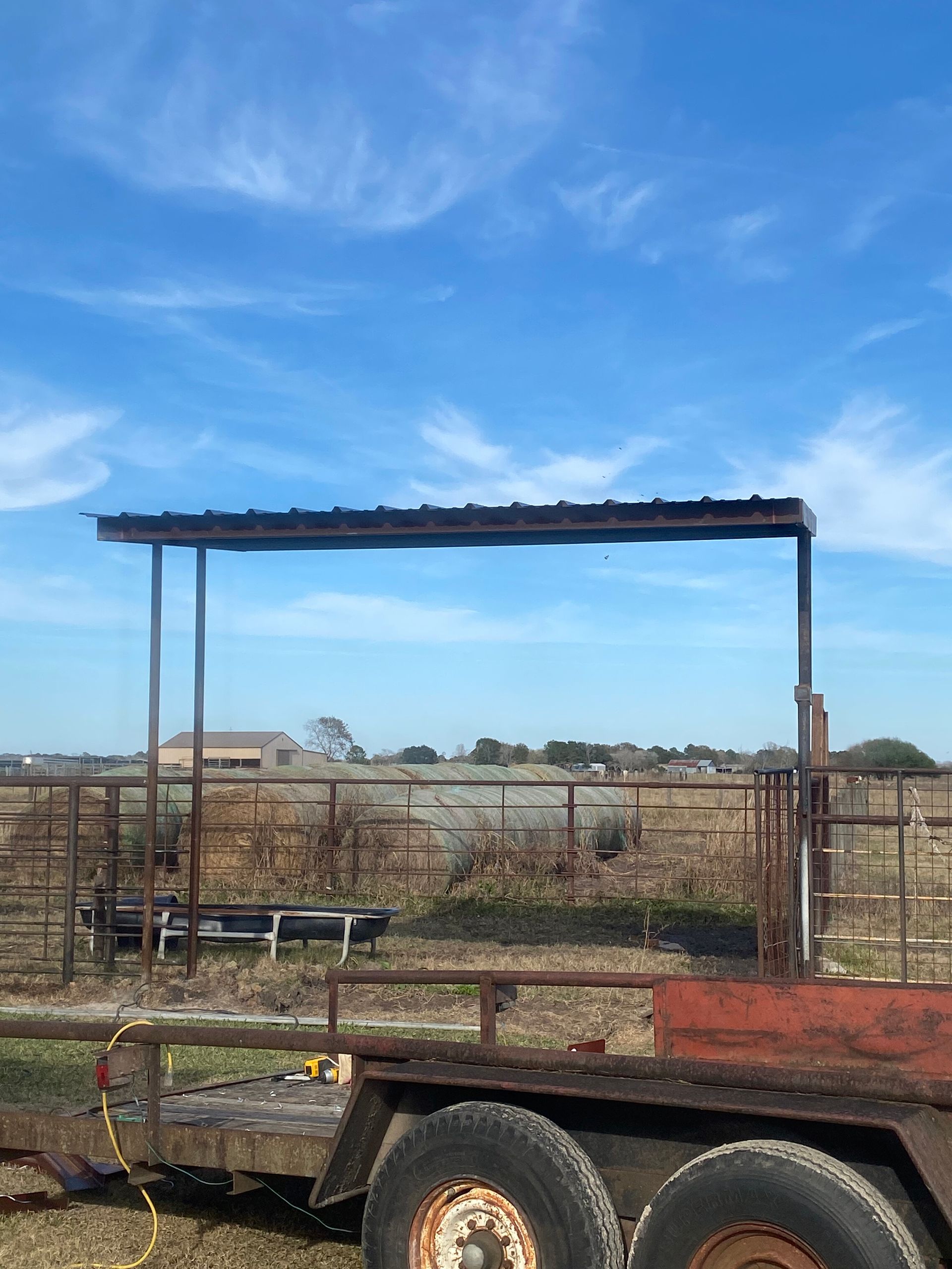 Rusted farm trailer with a metal frame under a blue sky in a rural field
