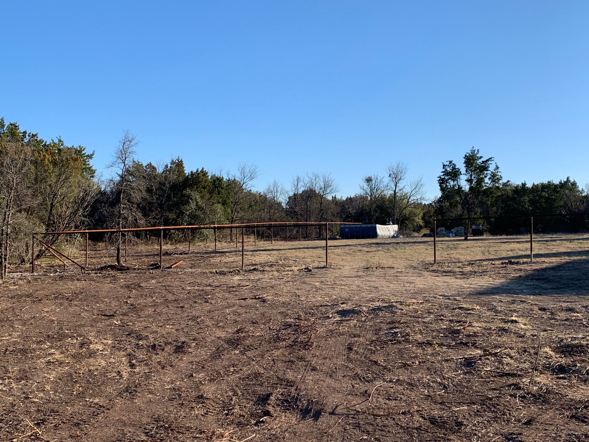 Dry open field with sparse trees, a low fence, and a clear blue sky.