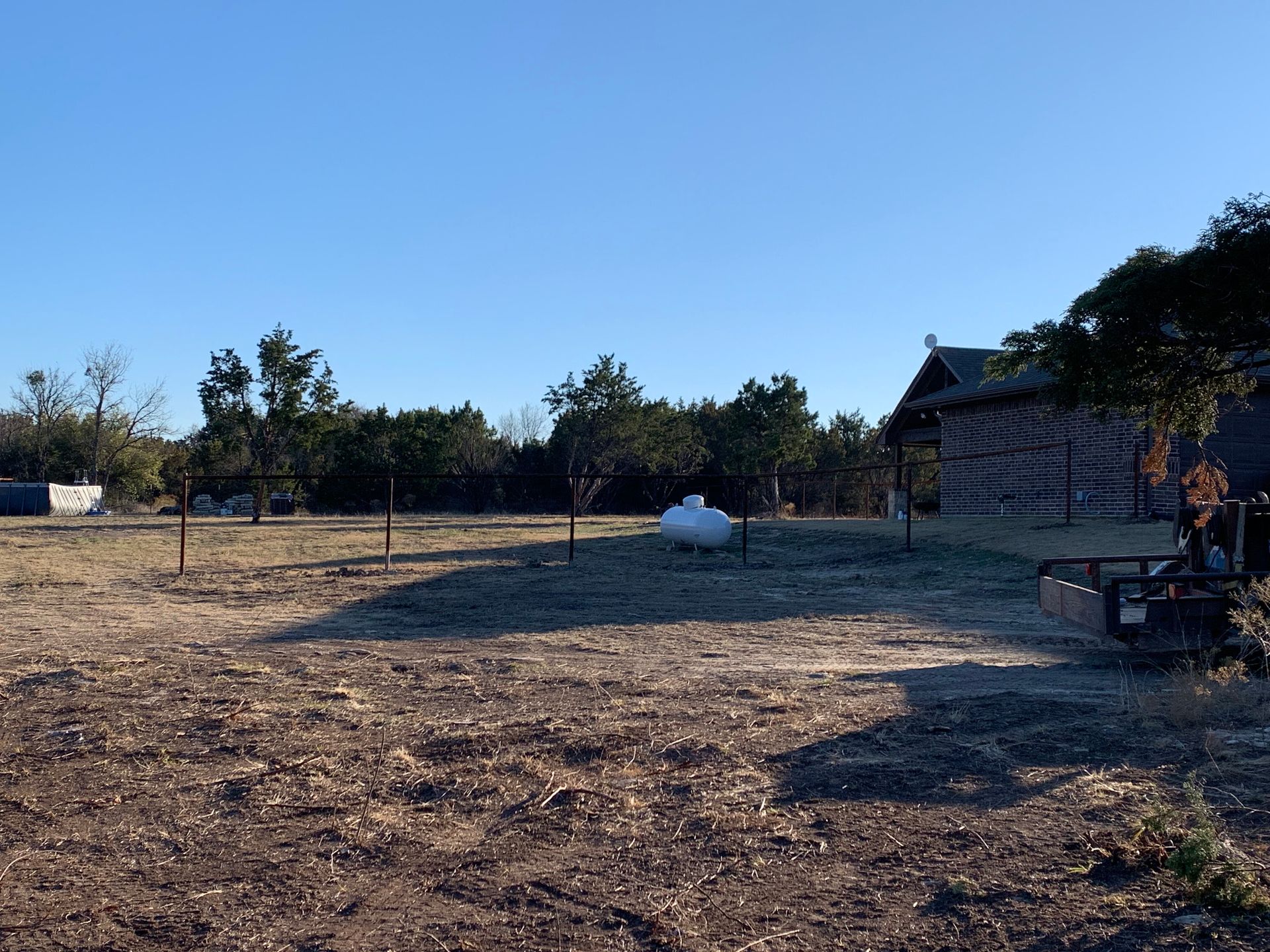 Open field with trees, a small shed, and a cart under a clear blue sky