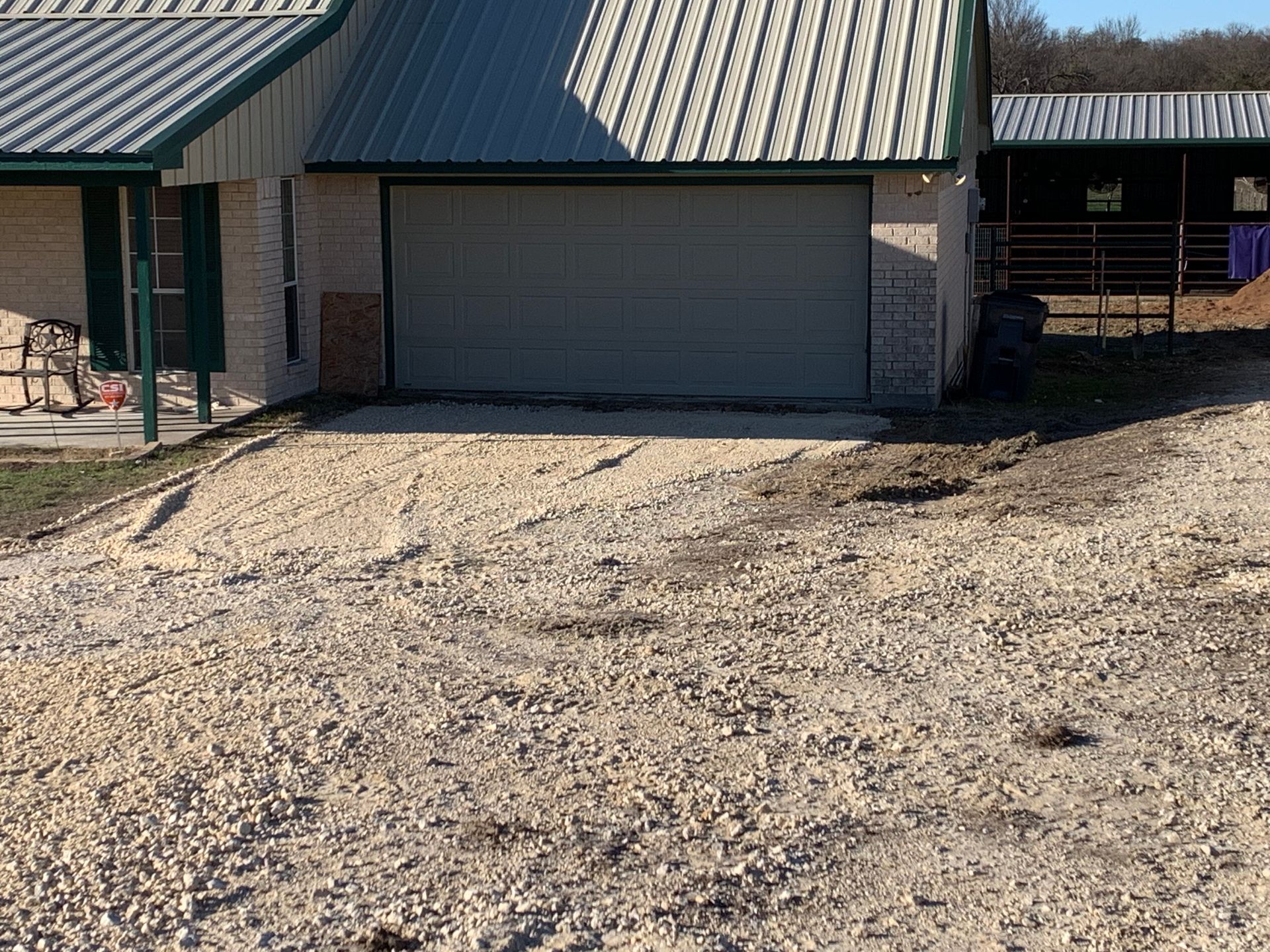Gravel driveway leading to a house with a green roof and closed garage door