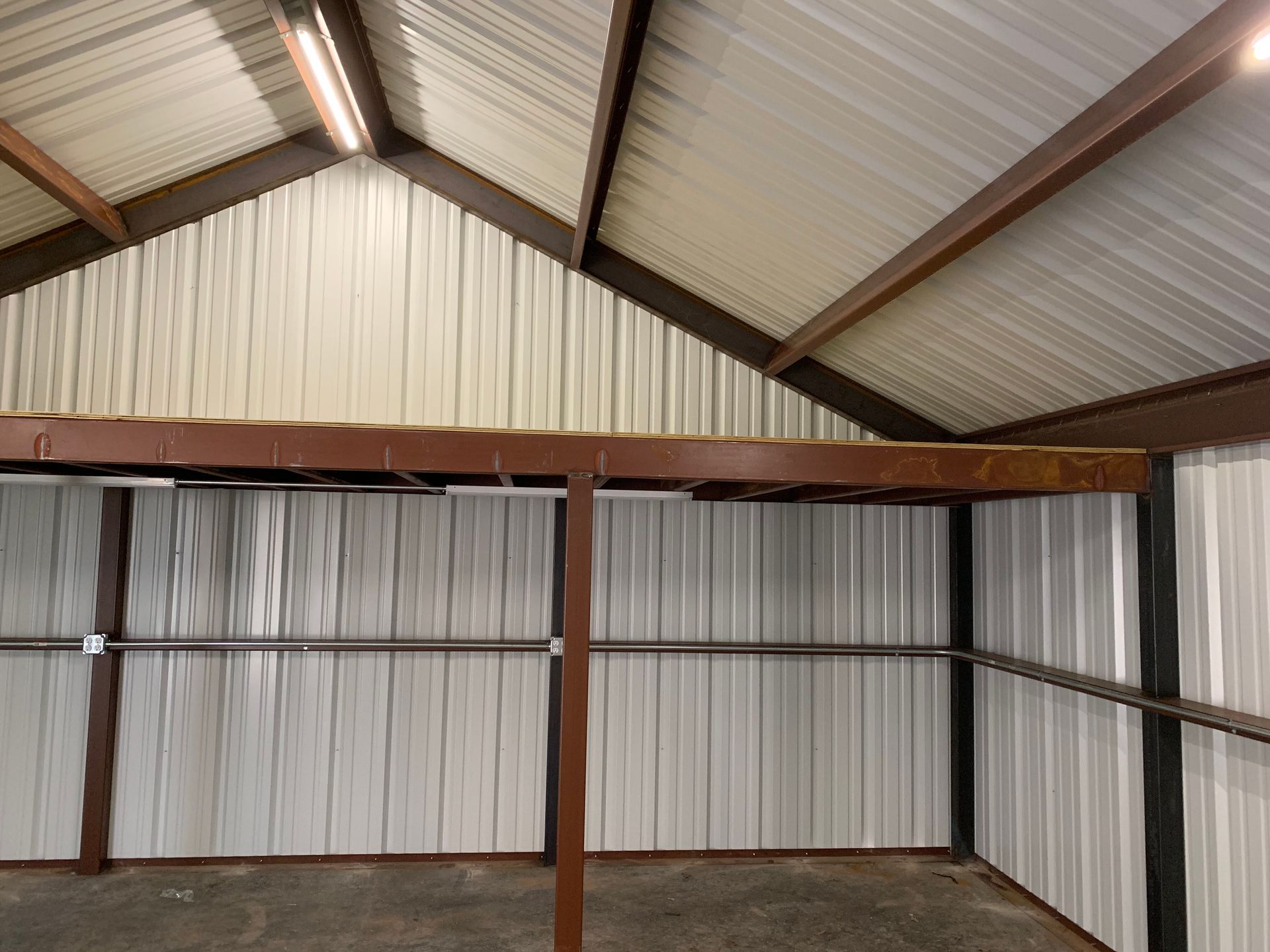 Empty metal storage shed interior with corrugated walls, roof beams, and overhead lighting