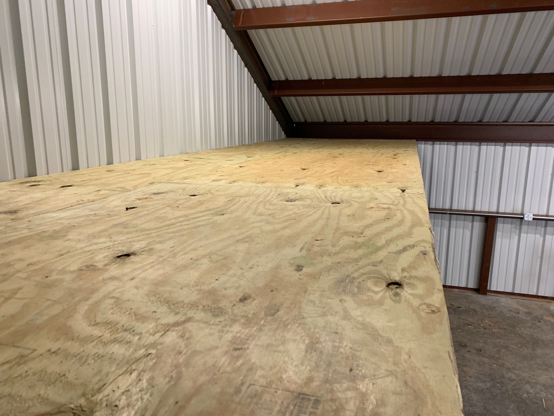 Plywood sheet leaning against the wall inside a metal-roofed workshop or barn.