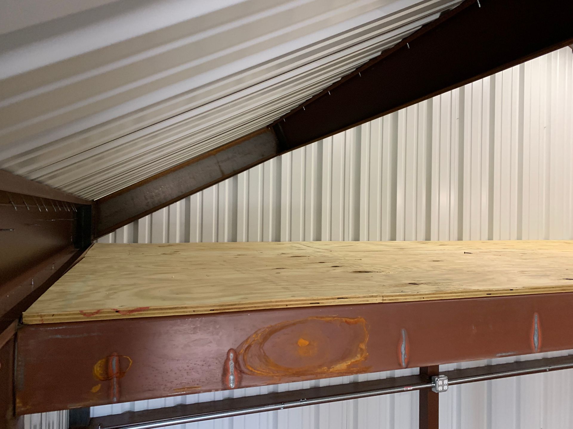 Loft storage area with corrugated metal walls, slanted roof, and a wooden platform above a brown beam