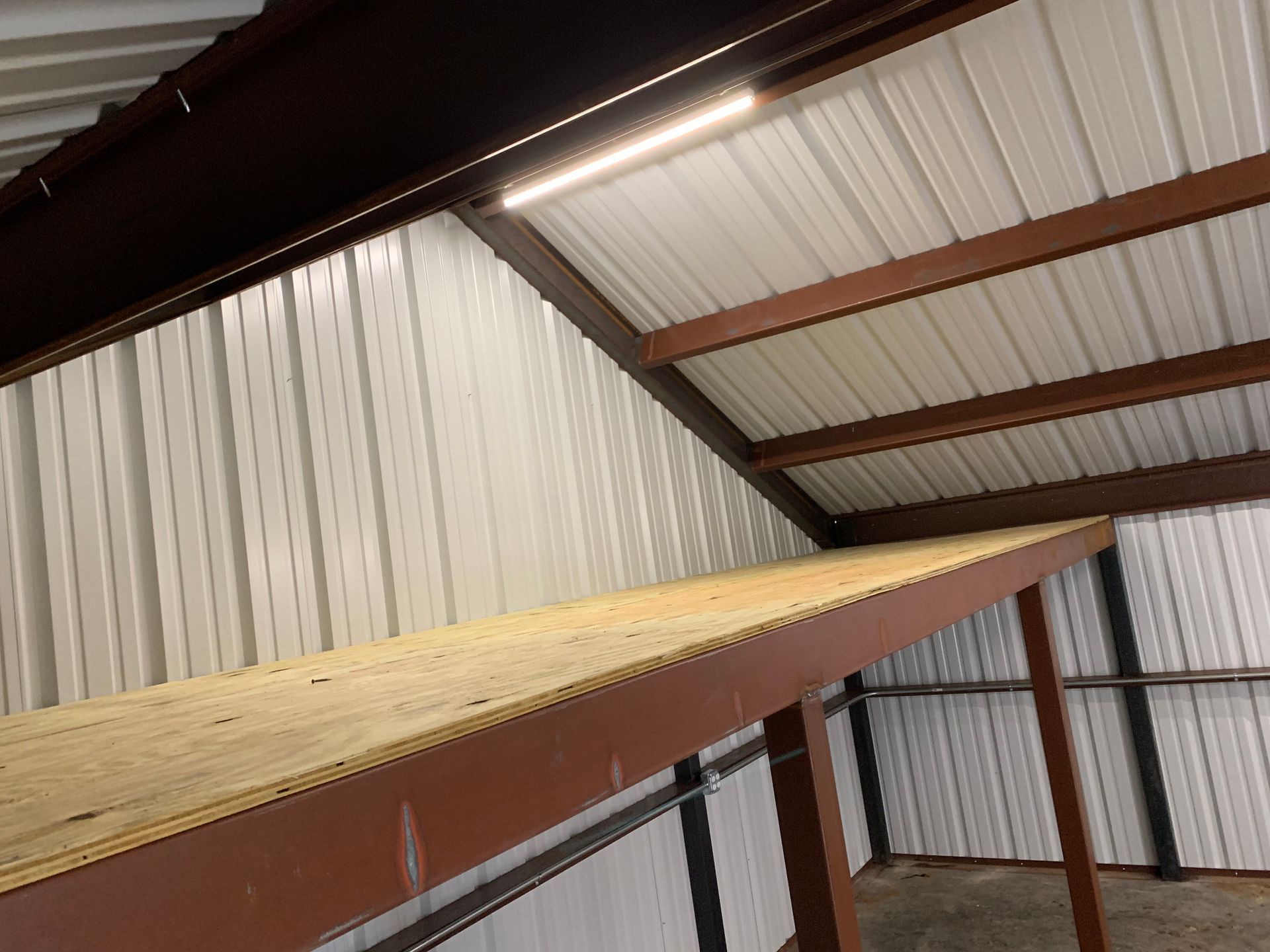 Long wooden shelf inside a metal storage shed with corrugated walls and roof supports