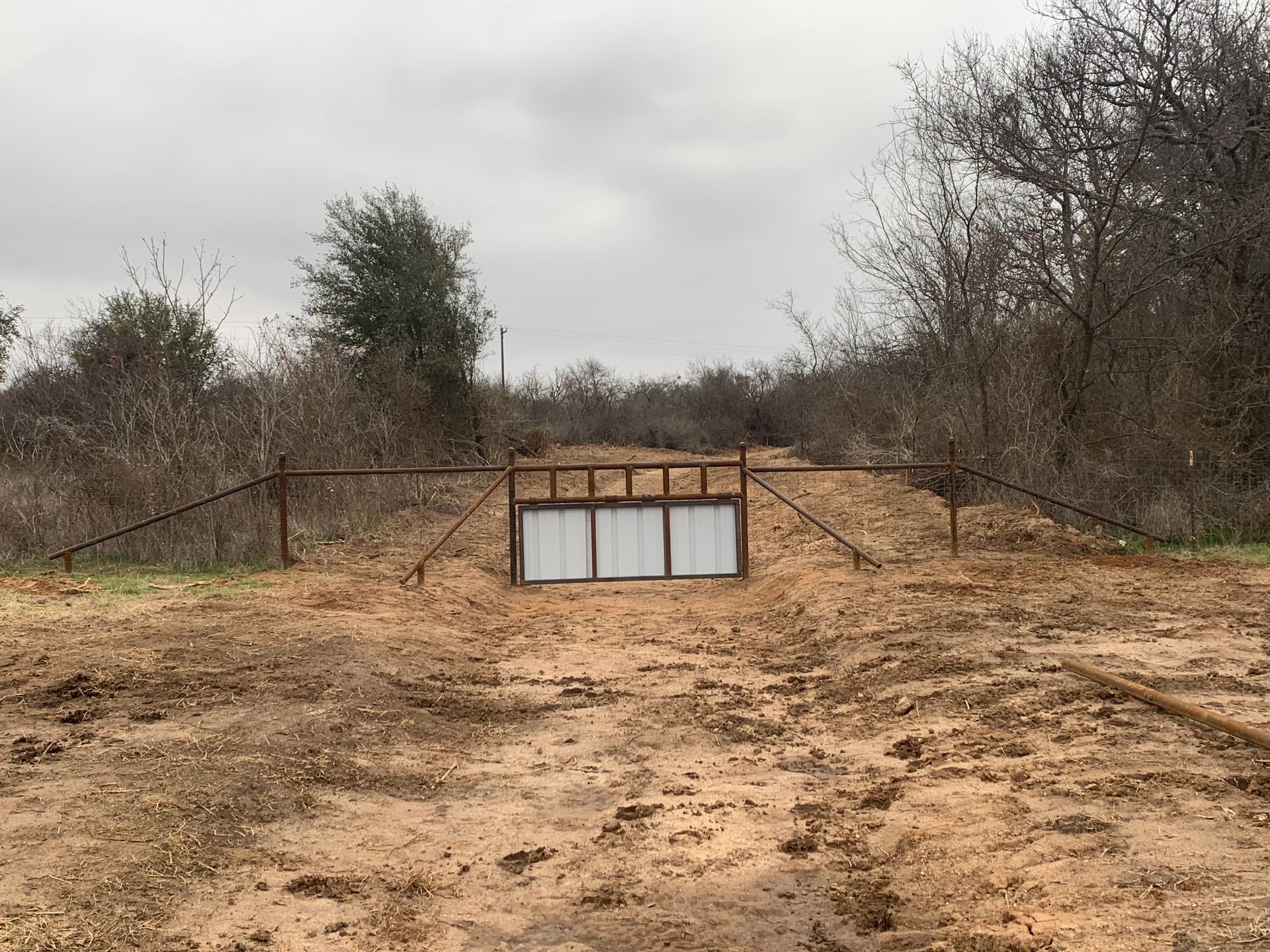 Small concrete-lined pit in a dry, brushy field under an overcast sky