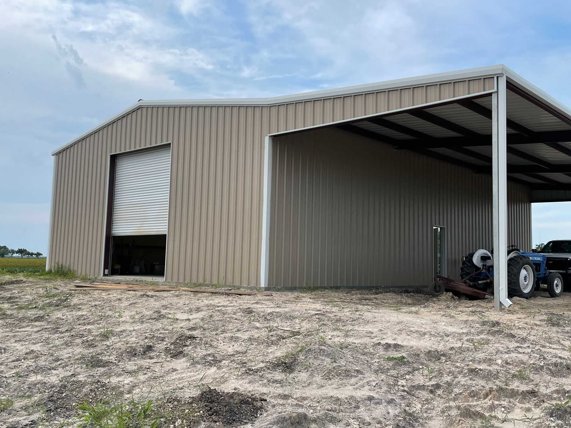 Metal farm shed with open bay and a tractor parked inside on a gravel lot