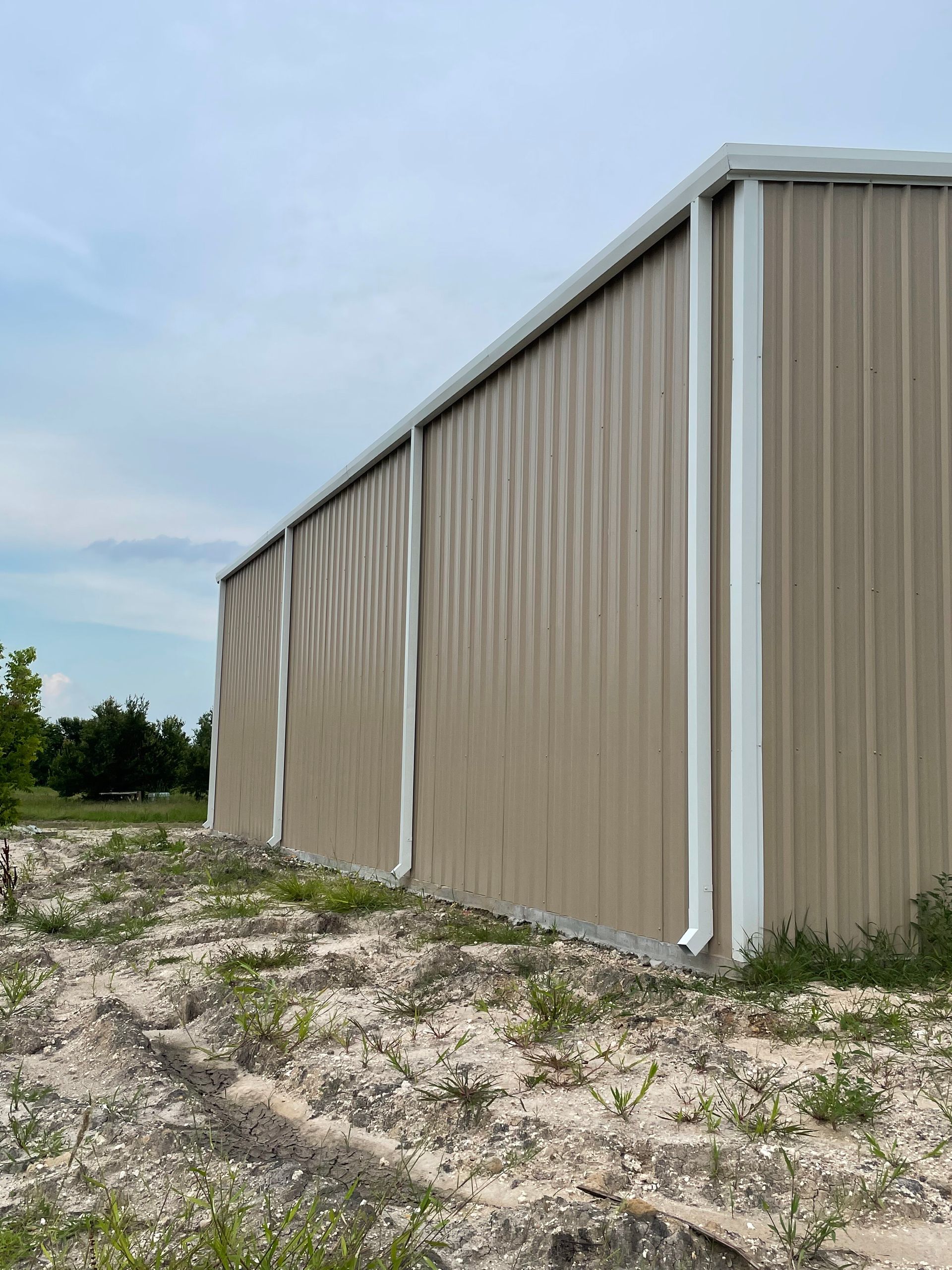 Tan metal-sided building on a gravel lot under a cloudy sky