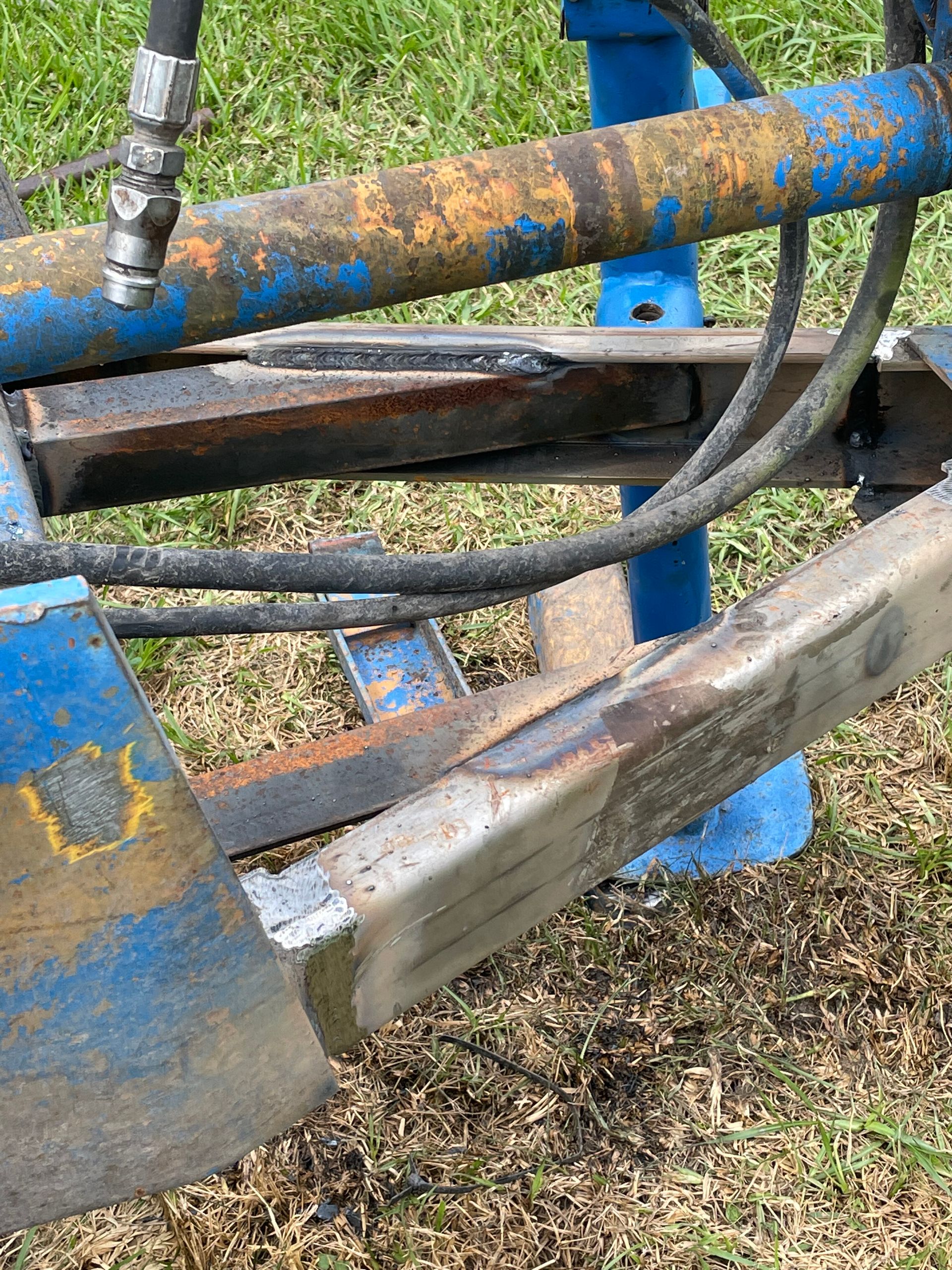 Rusty blue farm machinery with hydraulic hoses and a metal arm close-up outdoors