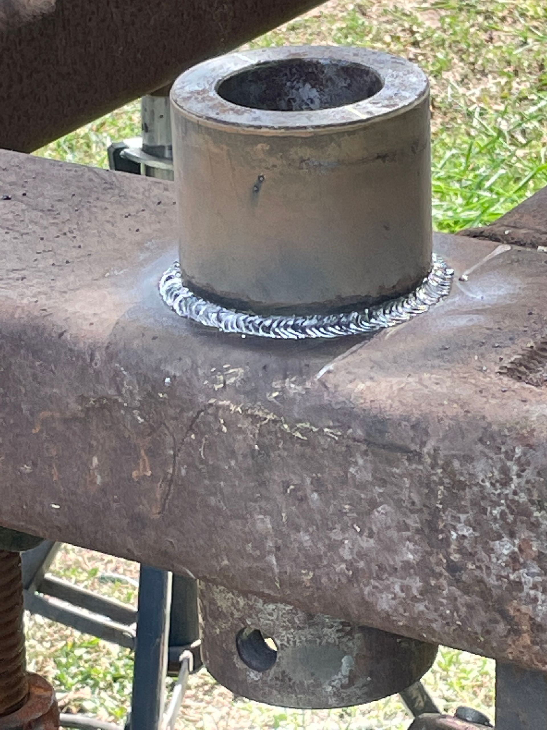 Welded metal bushing on a rusted steel beam outdoors, with grass visible in the background.