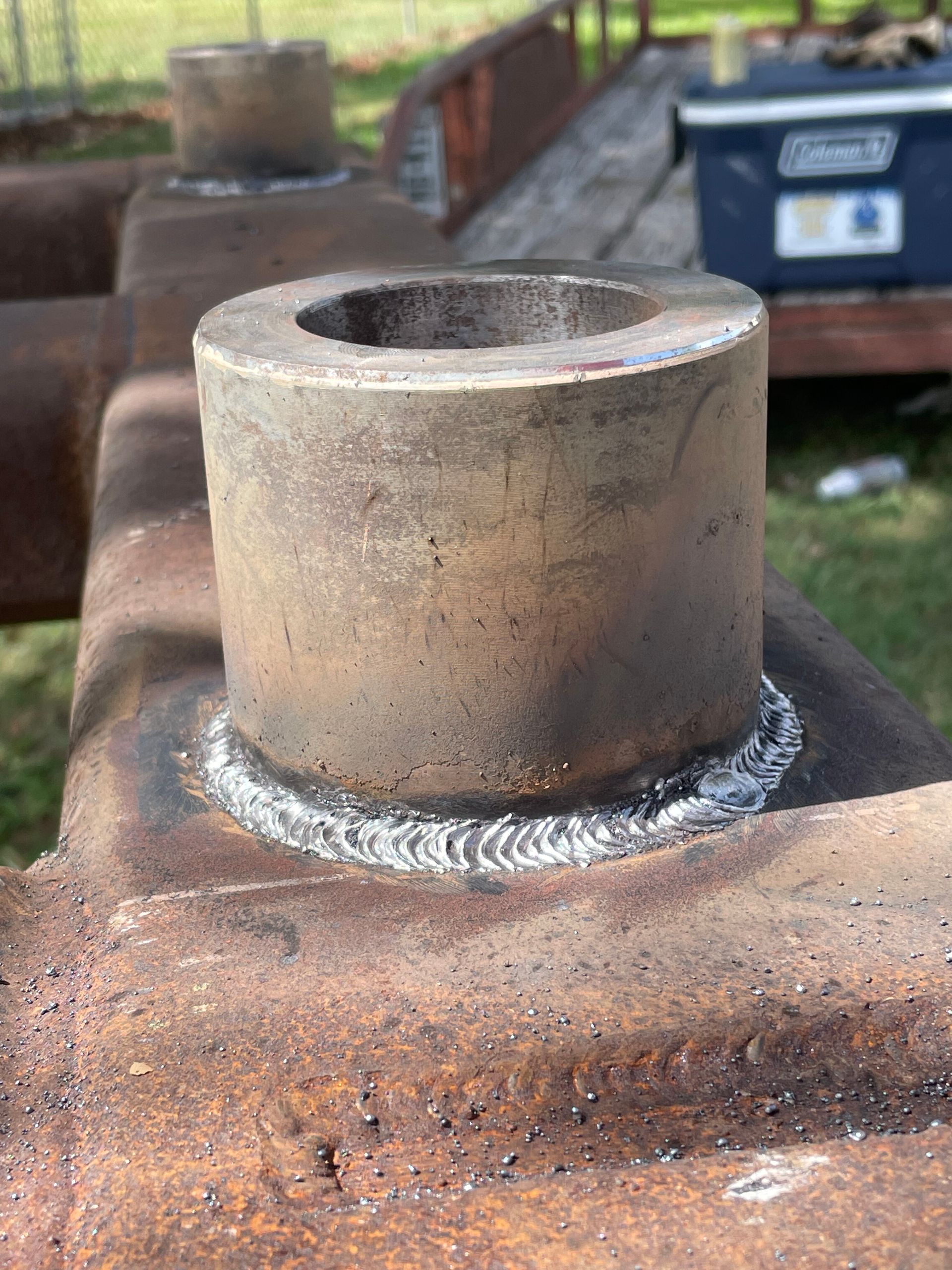 Close-up of a welded metal pipe fitting on a rusty steel surface outdoors.
