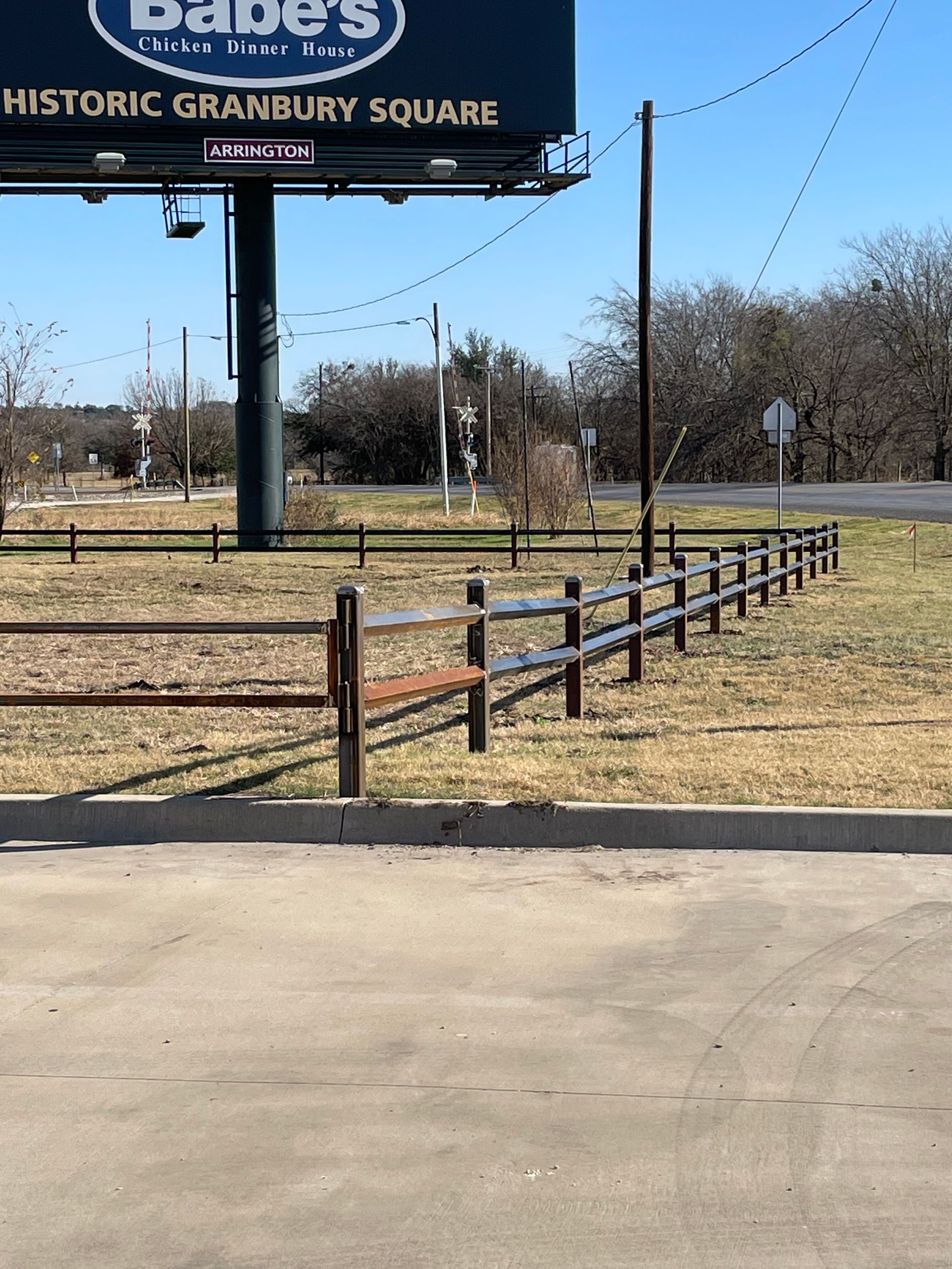 Empty roadside lot with a Babe's Historic Granbury Square sign and a low wooden fence under a clear sky