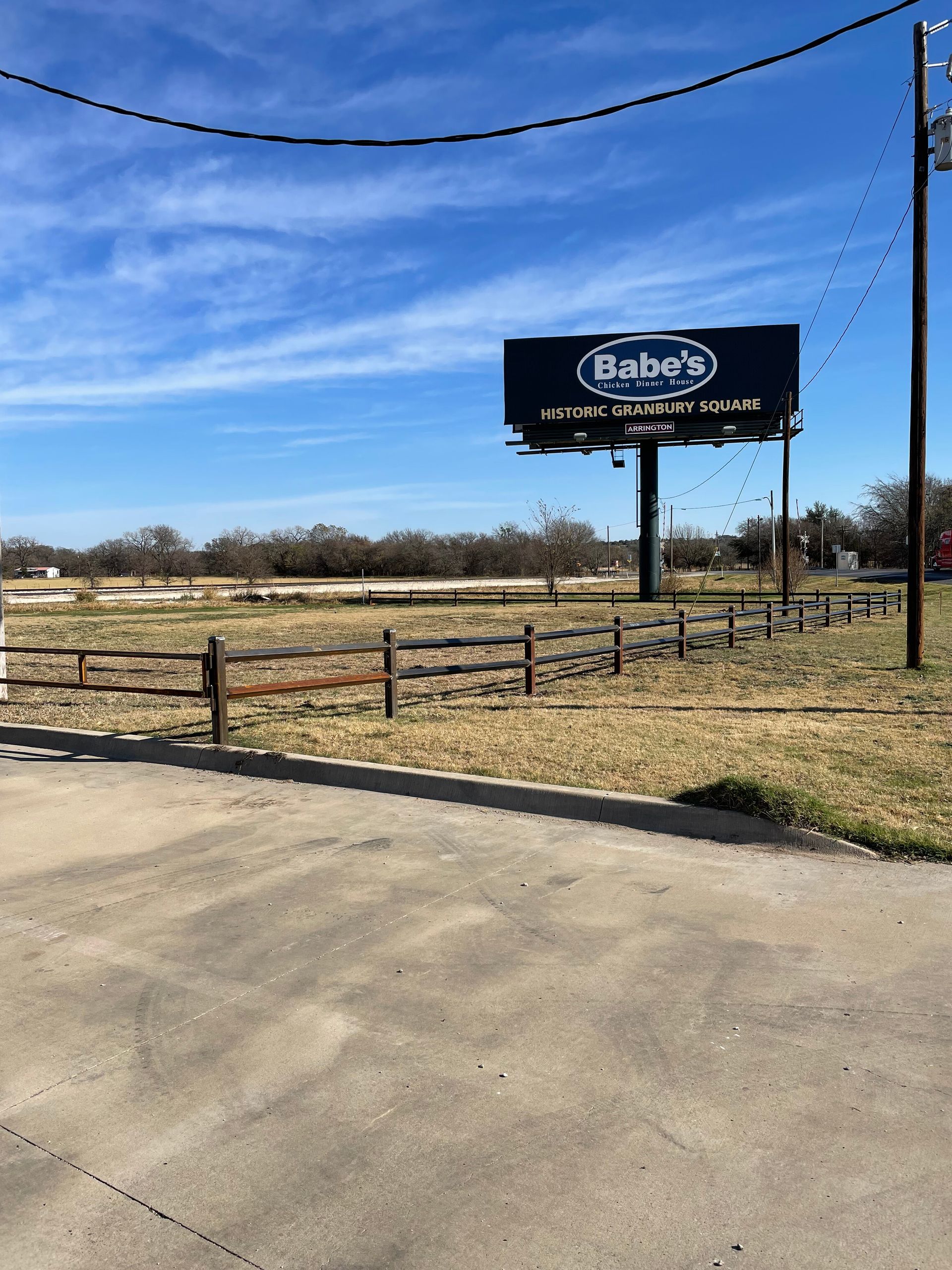 Rural roadside with a Bobo’s billboard, wooden fence, and open field under a blue sky
