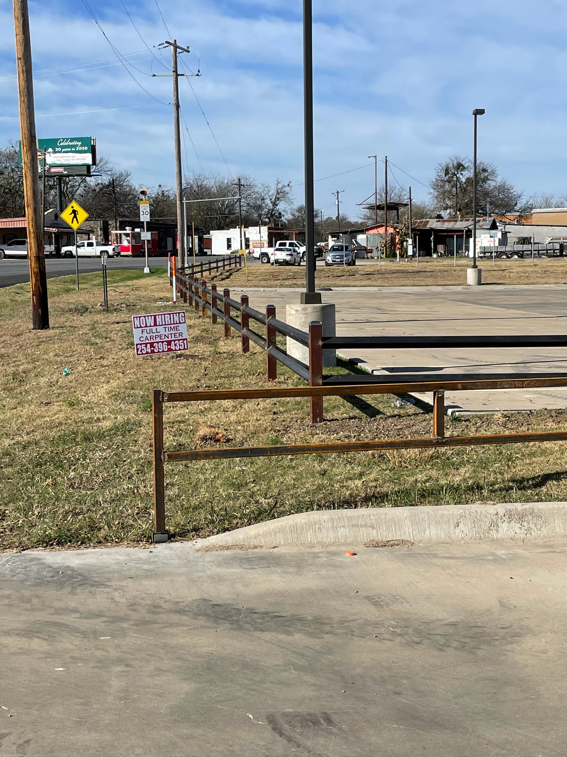 Rural roadside lot with a rusted fence, utility poles, and a small American flag sign near the curb.