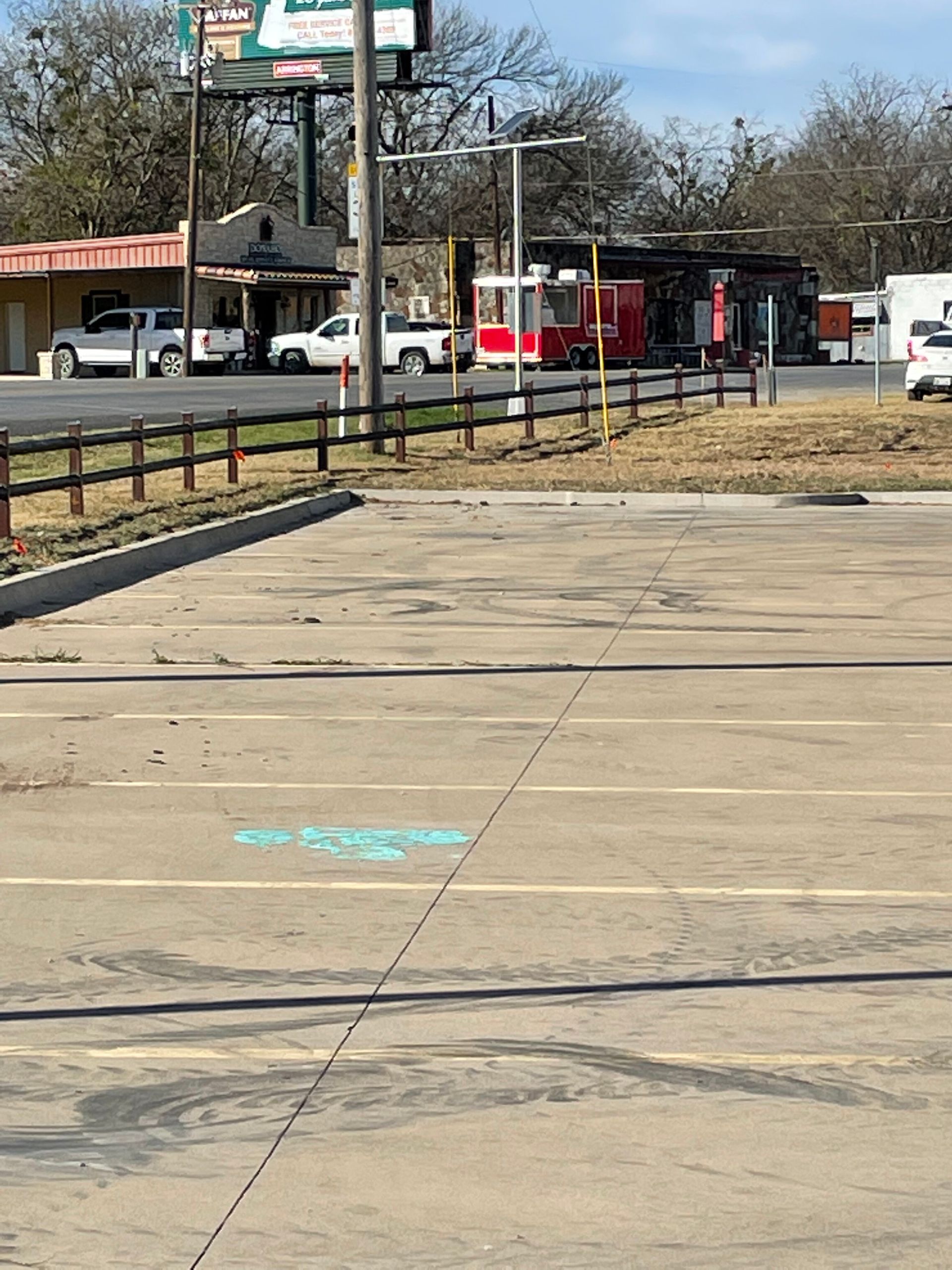 Empty parking lot with cracked pavement, orange cones, and buses along a roadside in the background