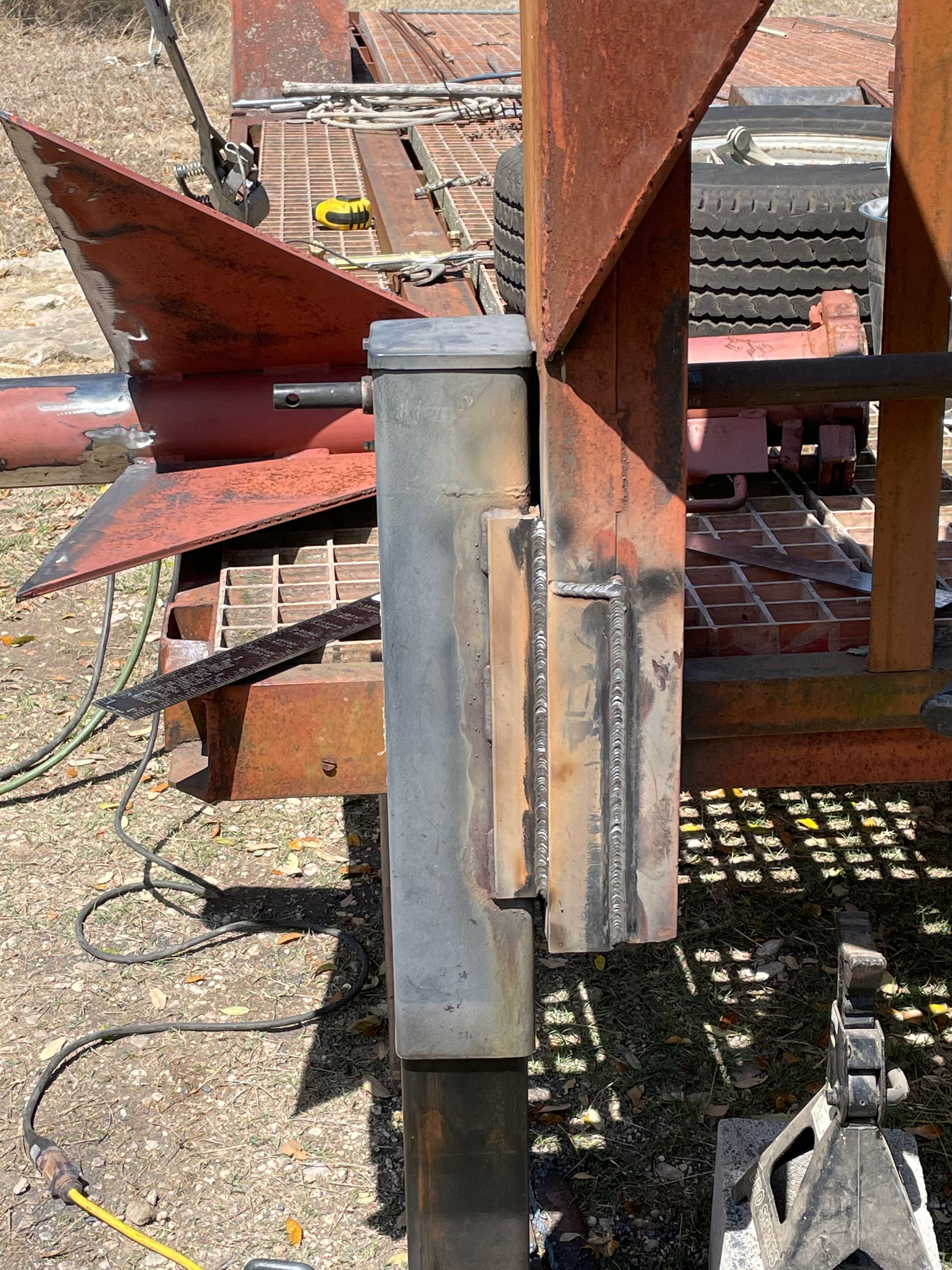 Rusty metal industrial machinery outdoors, showing a close-up of a welded steel joint and support beam.