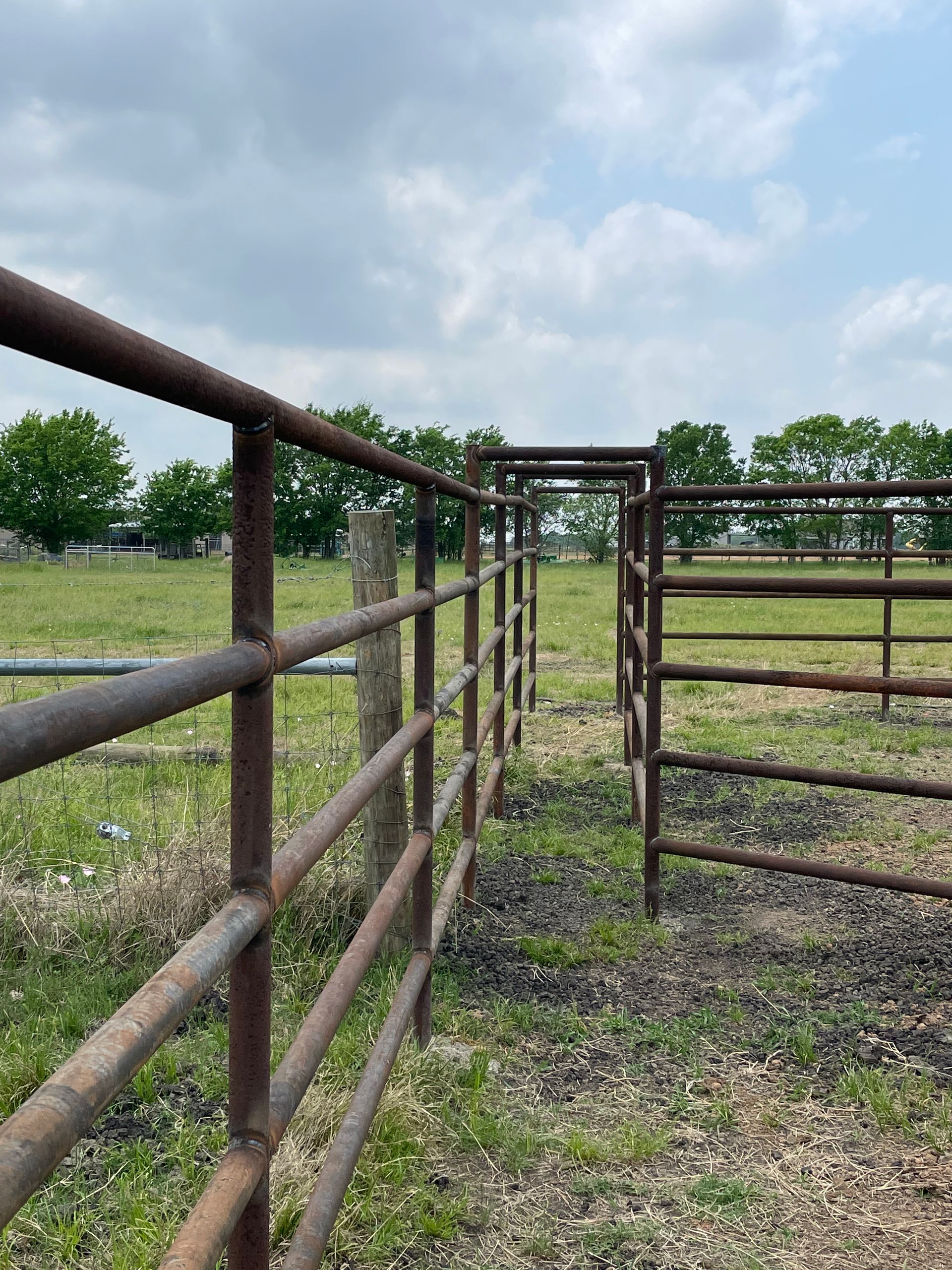 Rusty ranch fence and gate in a grassy field under a cloudy sky