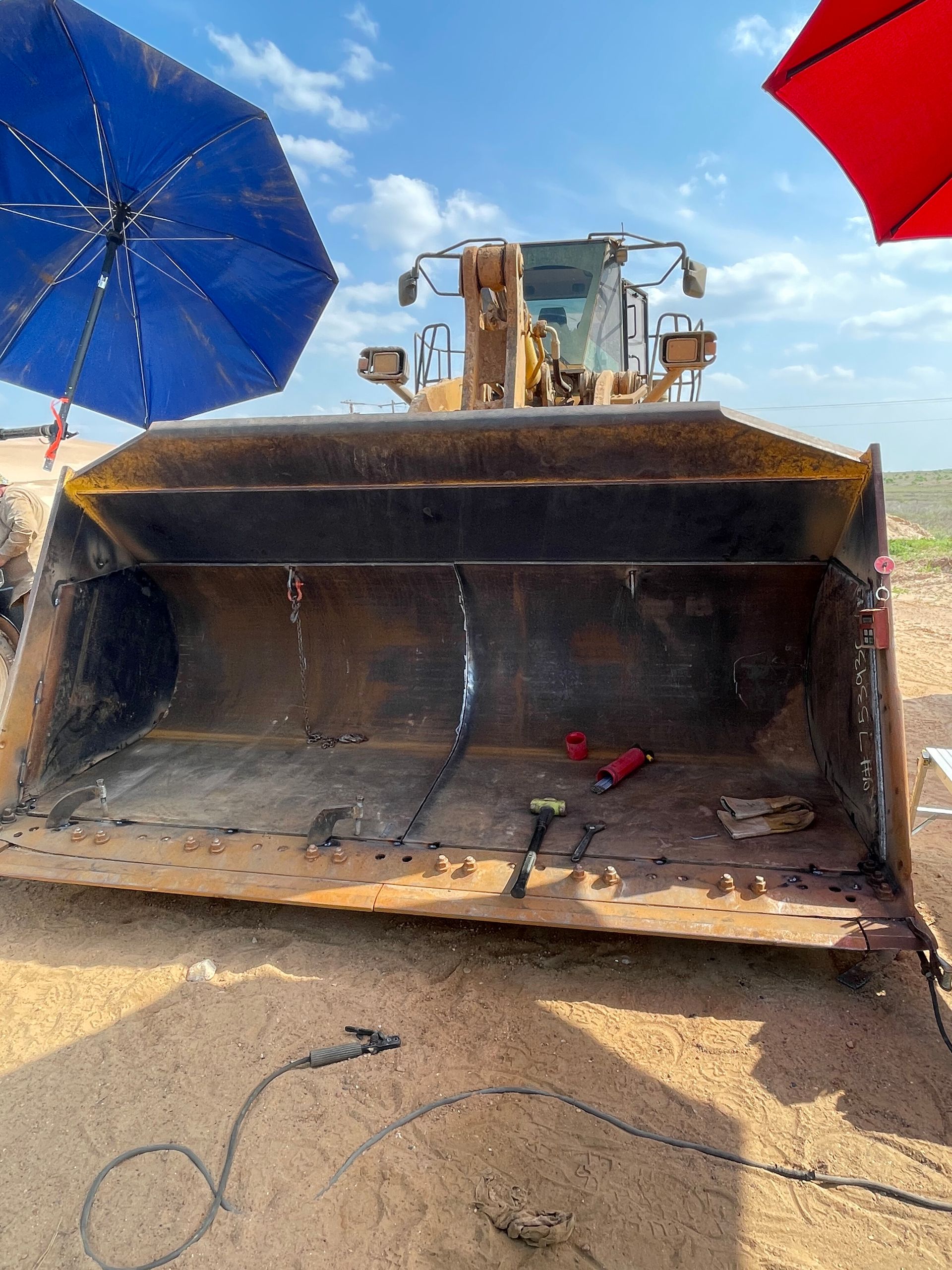 Large bulldozer bucket on a beach with colorful umbrellas and blue sky