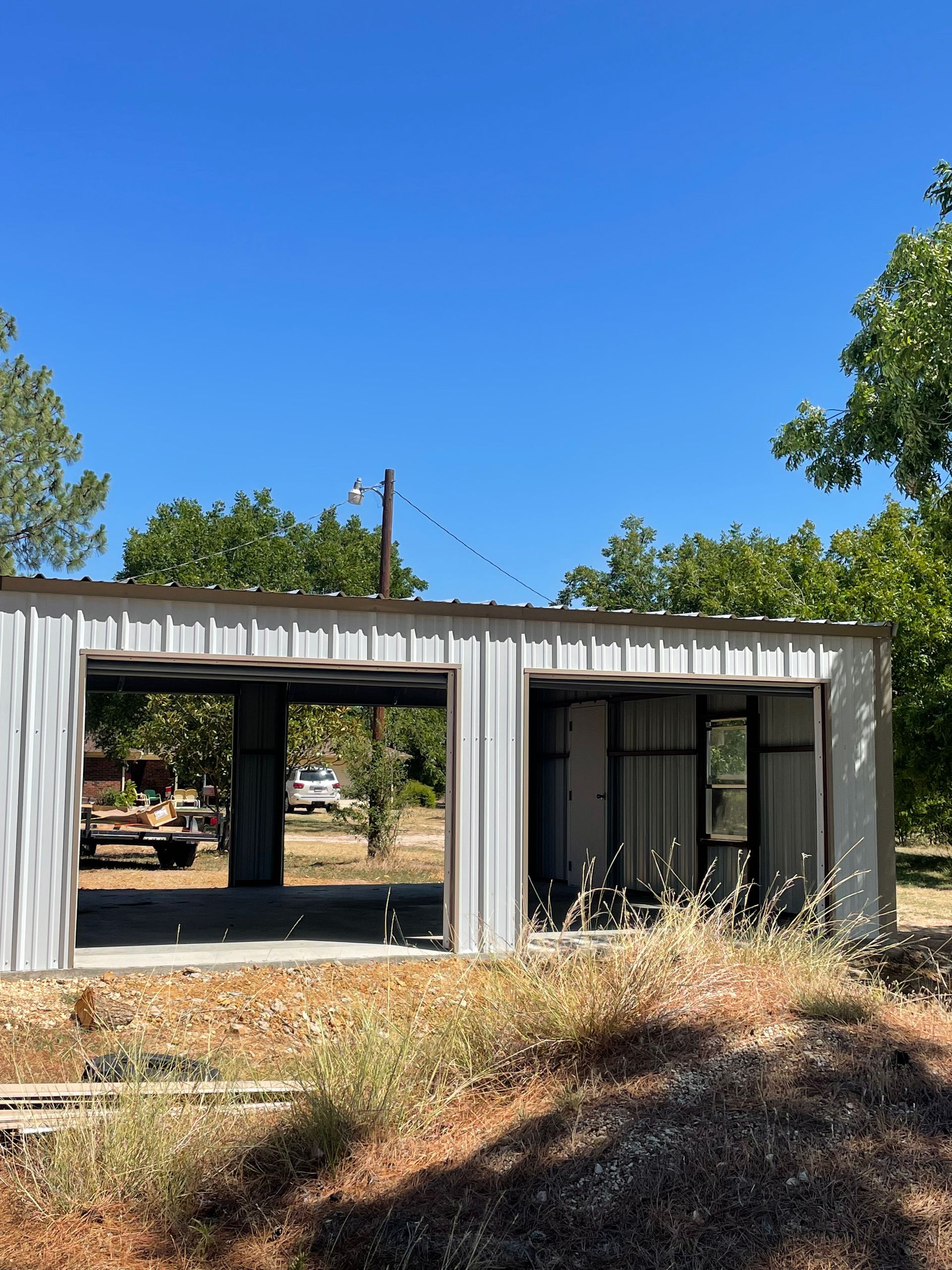 Modern gray house with large open windows and a glass door, surrounded by dry grass under a clear blue sky