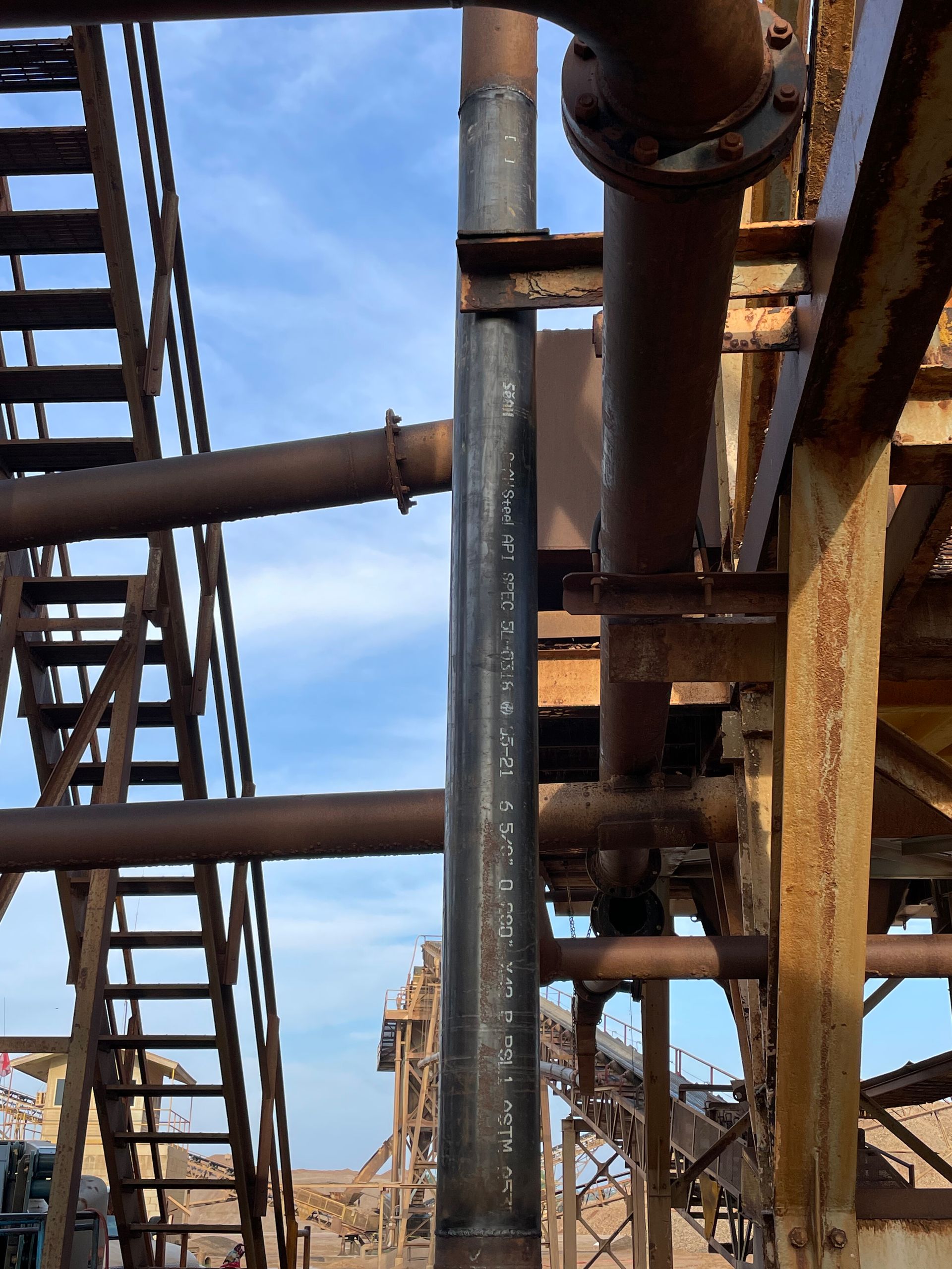 Rusty industrial pipes and metal stairs against a blue sky at an industrial site