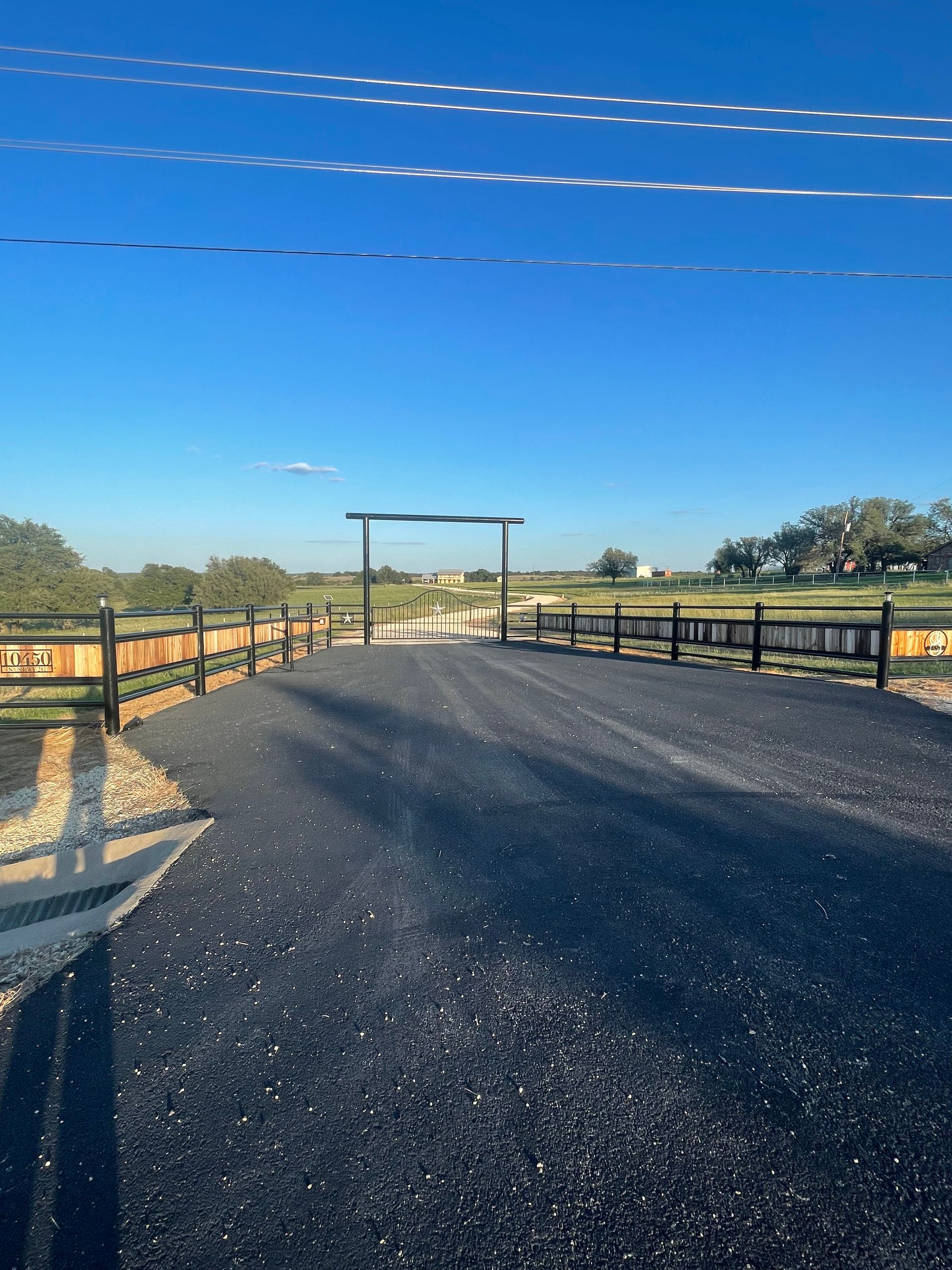 Rural paved road leading to a gated entrance under a clear blue sky