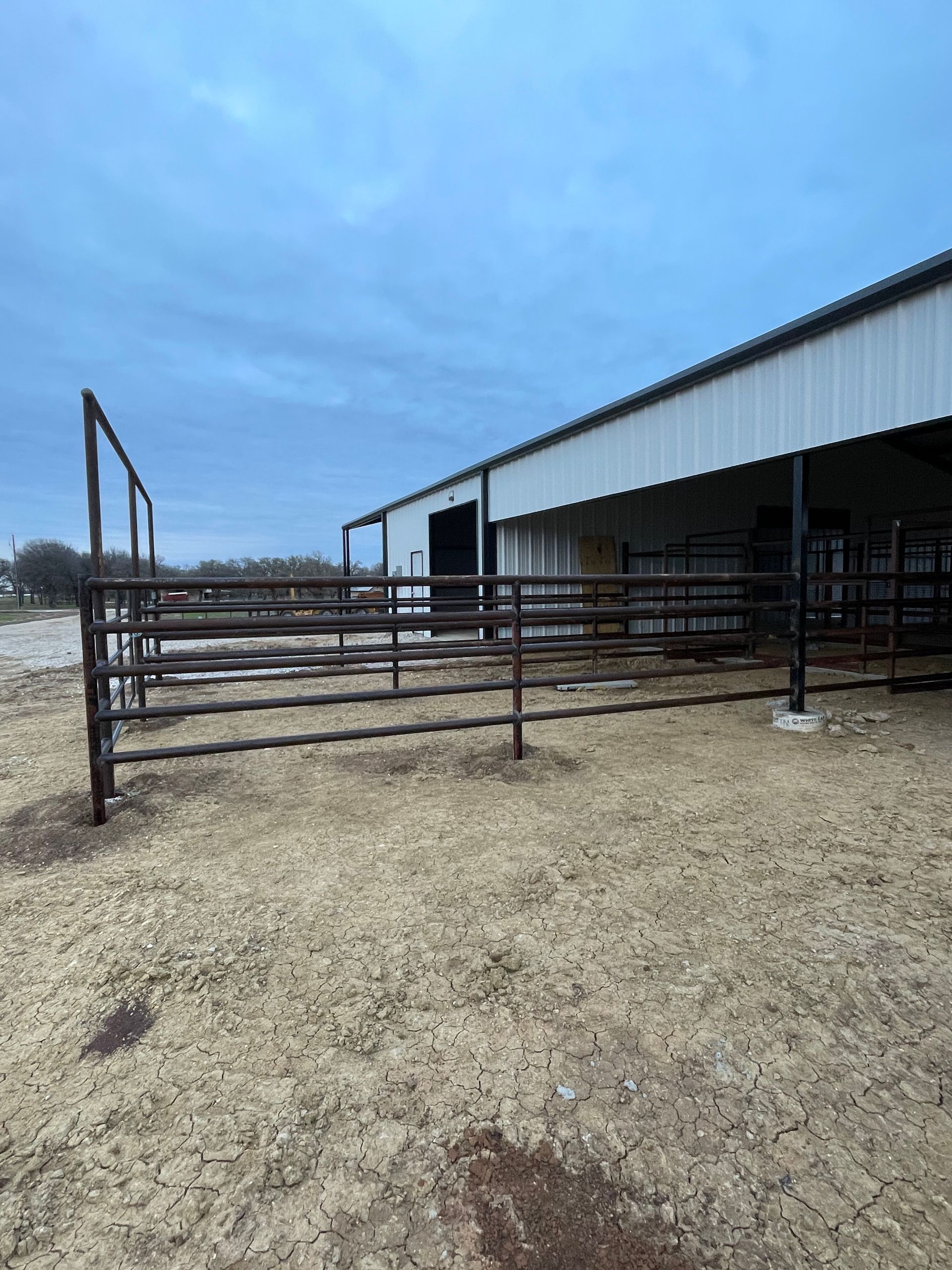 Fenced livestock pen beside a metal barn under a cloudy sky