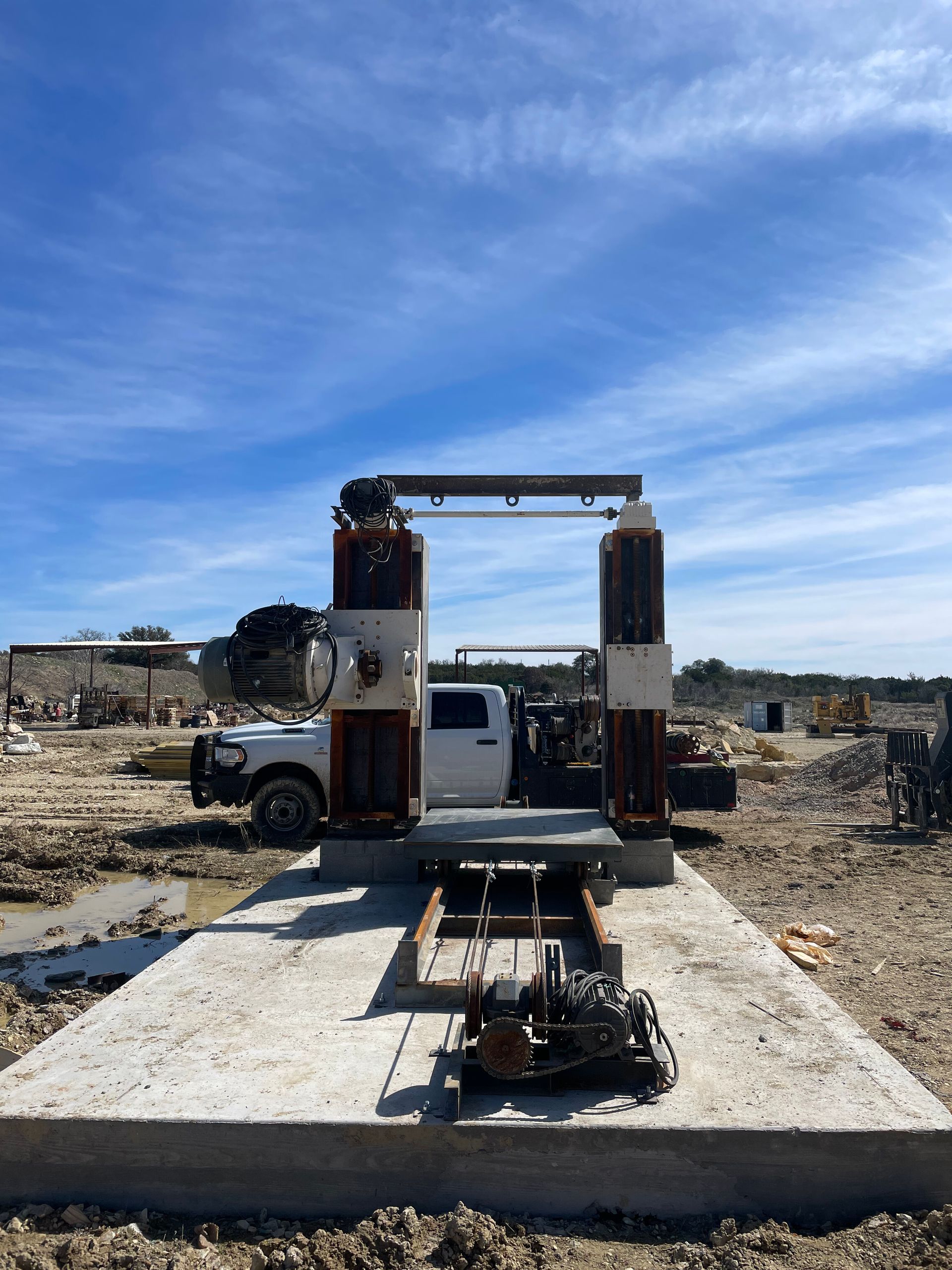 Damaged vehicle chassis on a concrete slab in a rubble-strewn lot under a blue sky