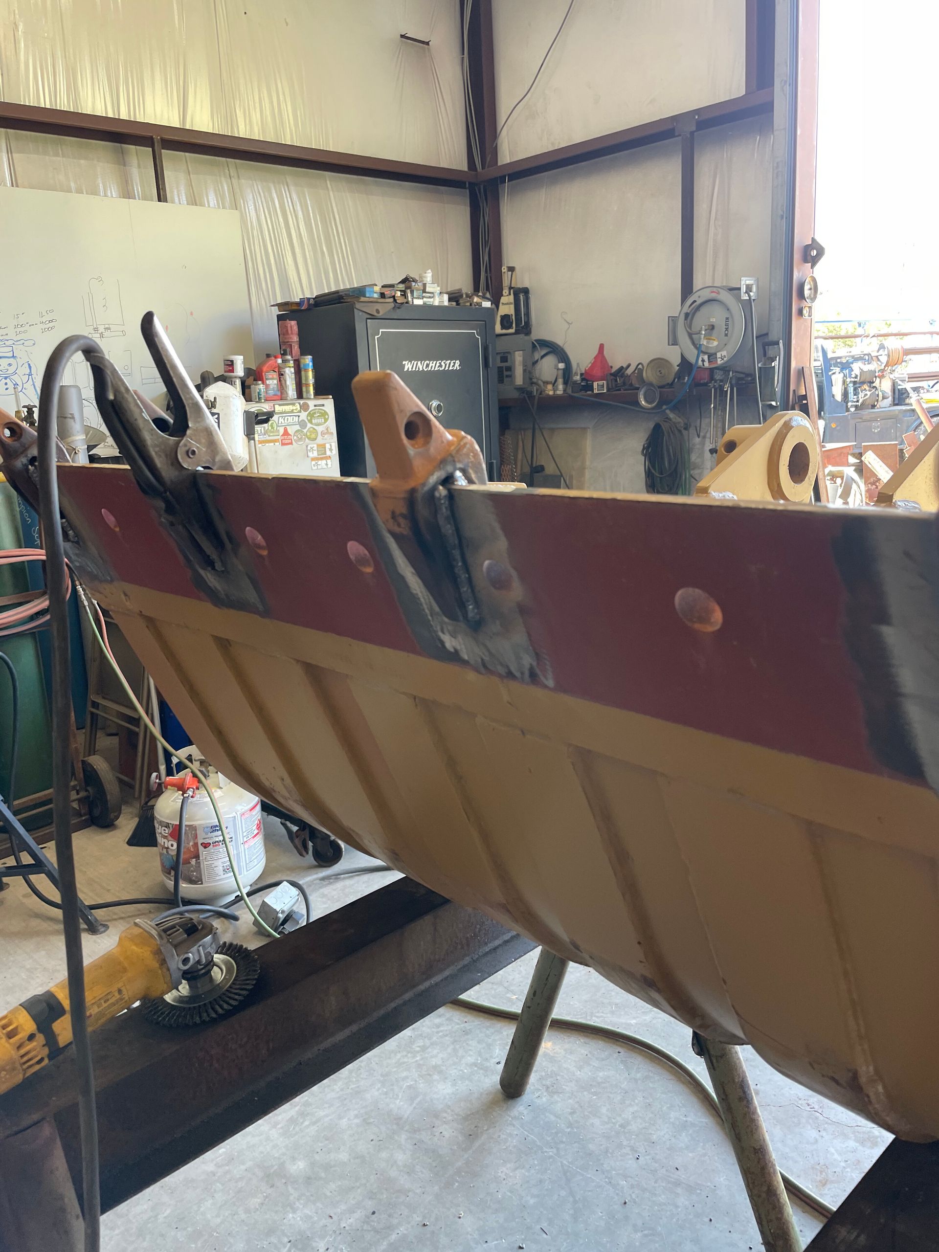 Large red-and-tan boat hull on stands inside a workshop, with tools and equipment in the background