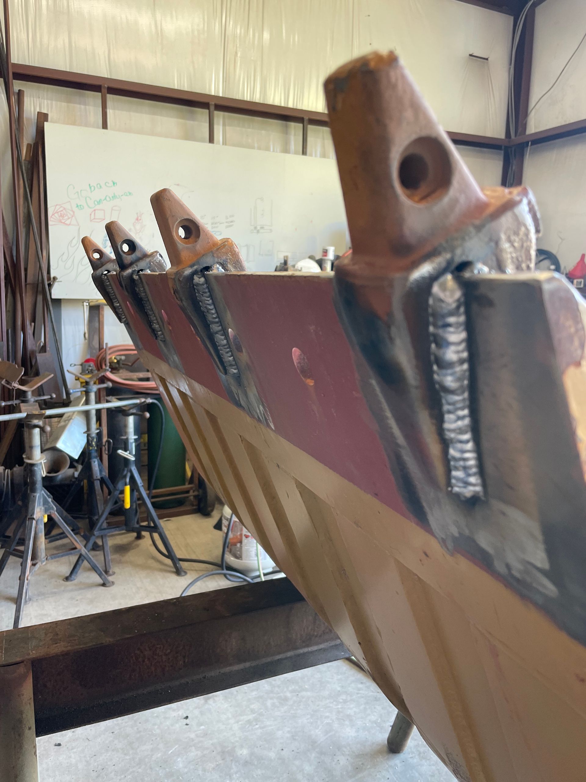 Boat hull under construction in a workshop, with welded metal brackets and orange supports.