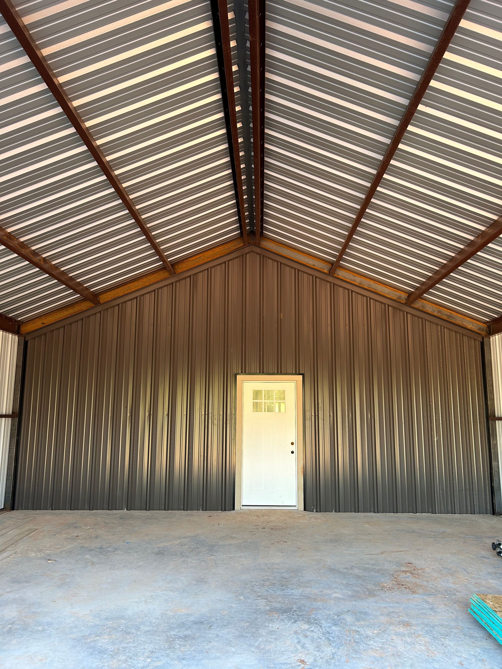 Empty metal barn interior with a white door on the far wall and a corrugated roof.