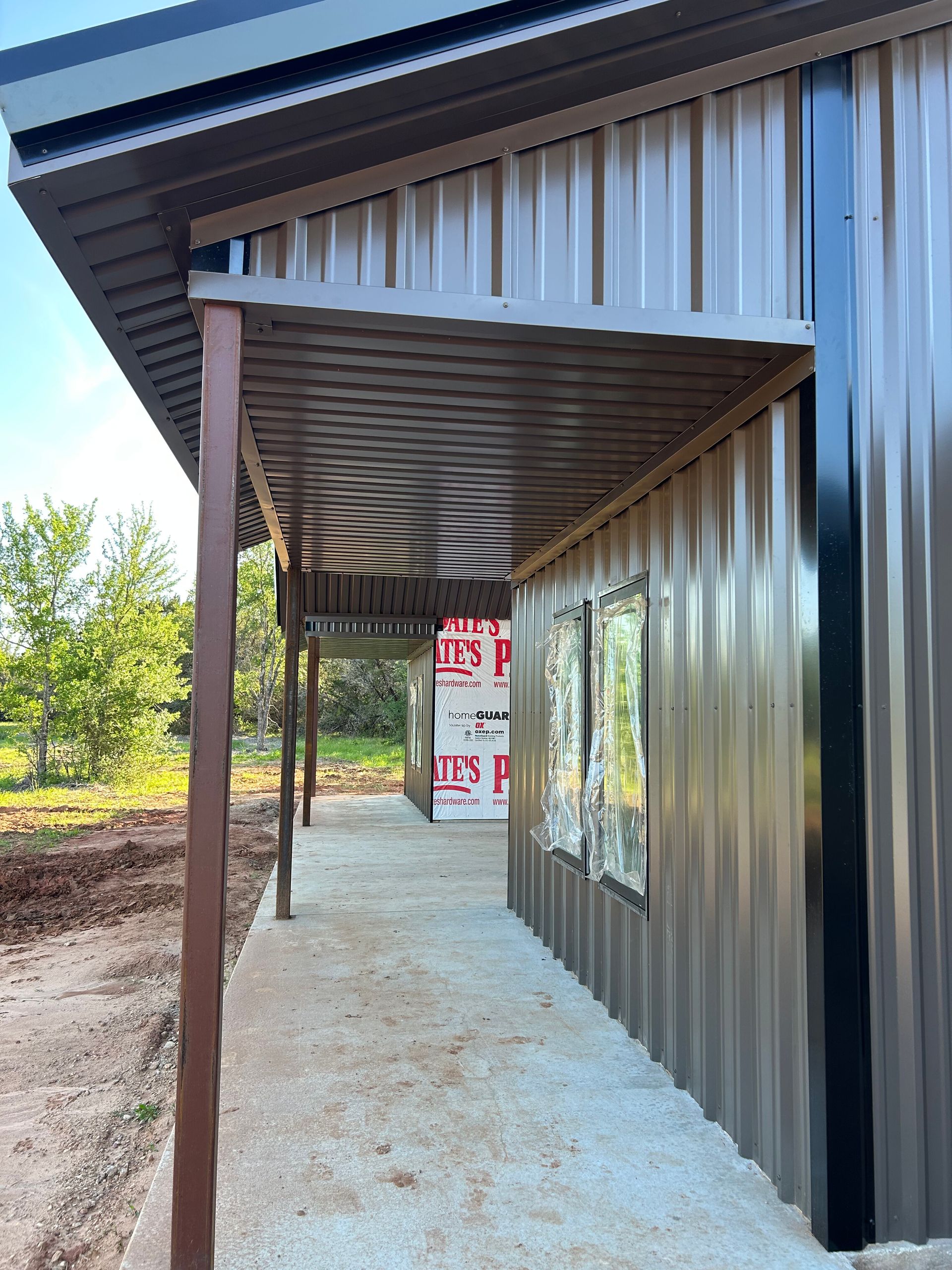 Corrugated metal porch on a modern building, with a concrete walkway and open fields in the background