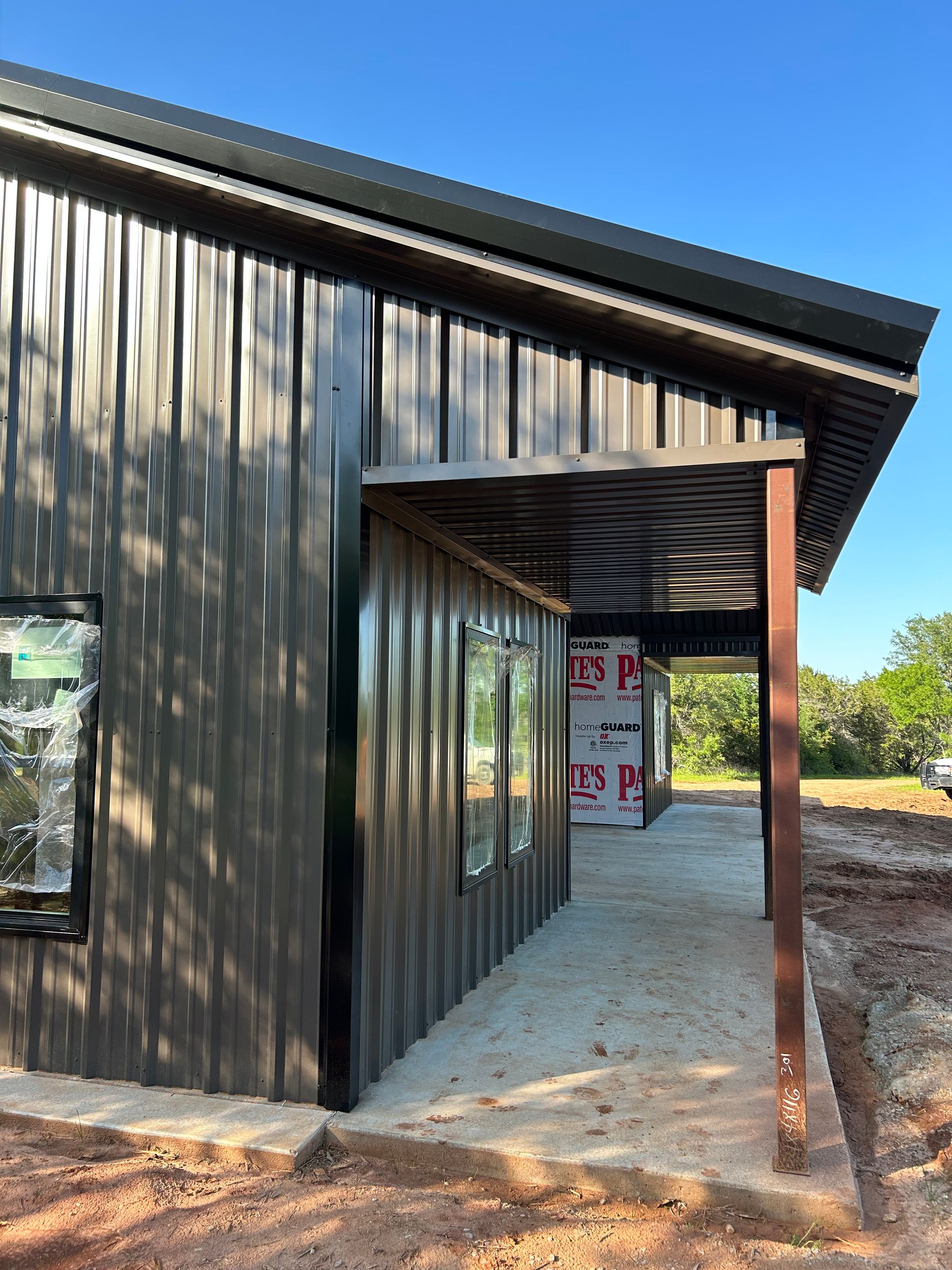 Black metal building with an open covered entry and gravel path on a sunny day