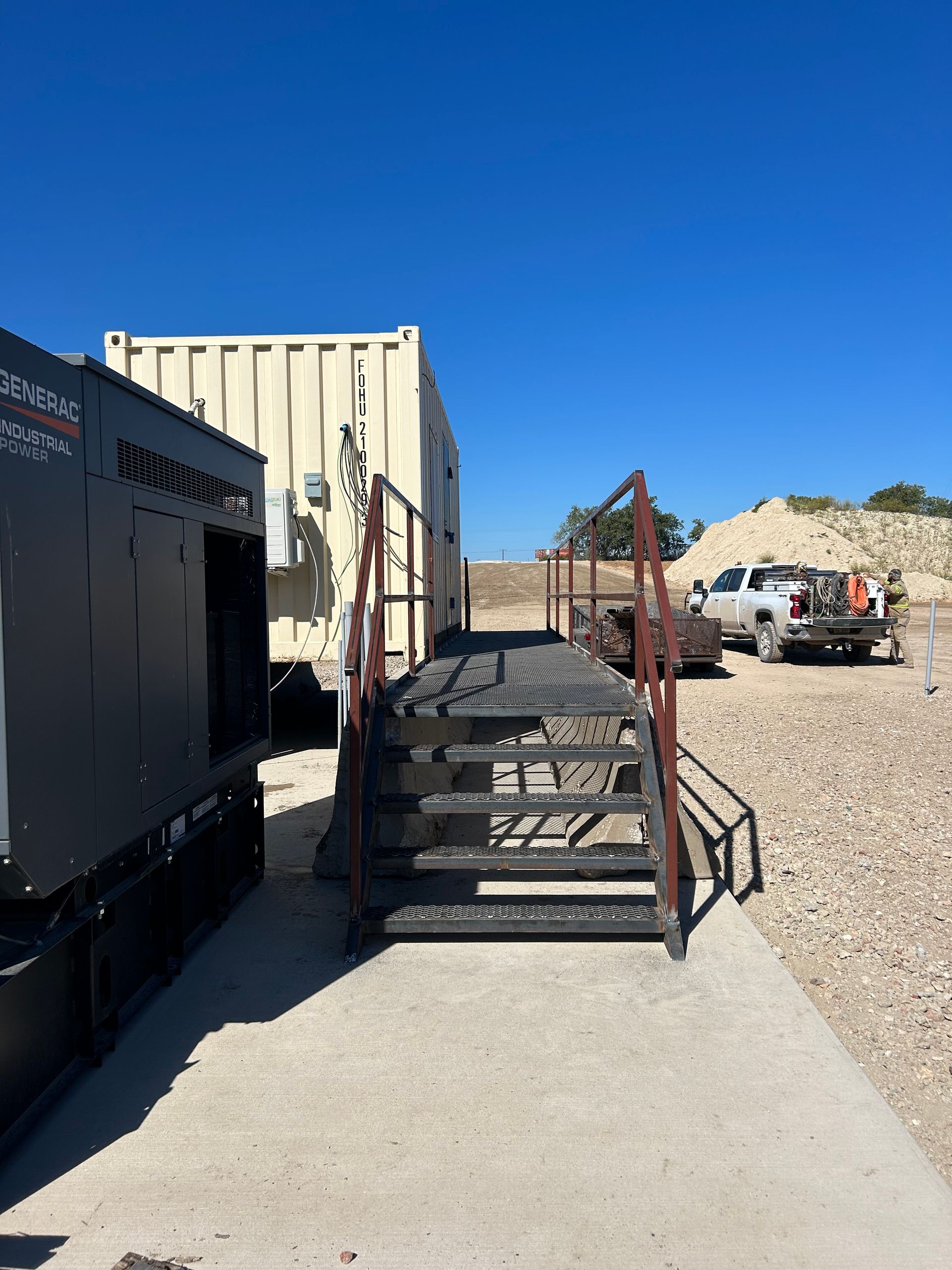 Industrial yard with a metal cage holding a covered object beside large equipment under a clear blue sky