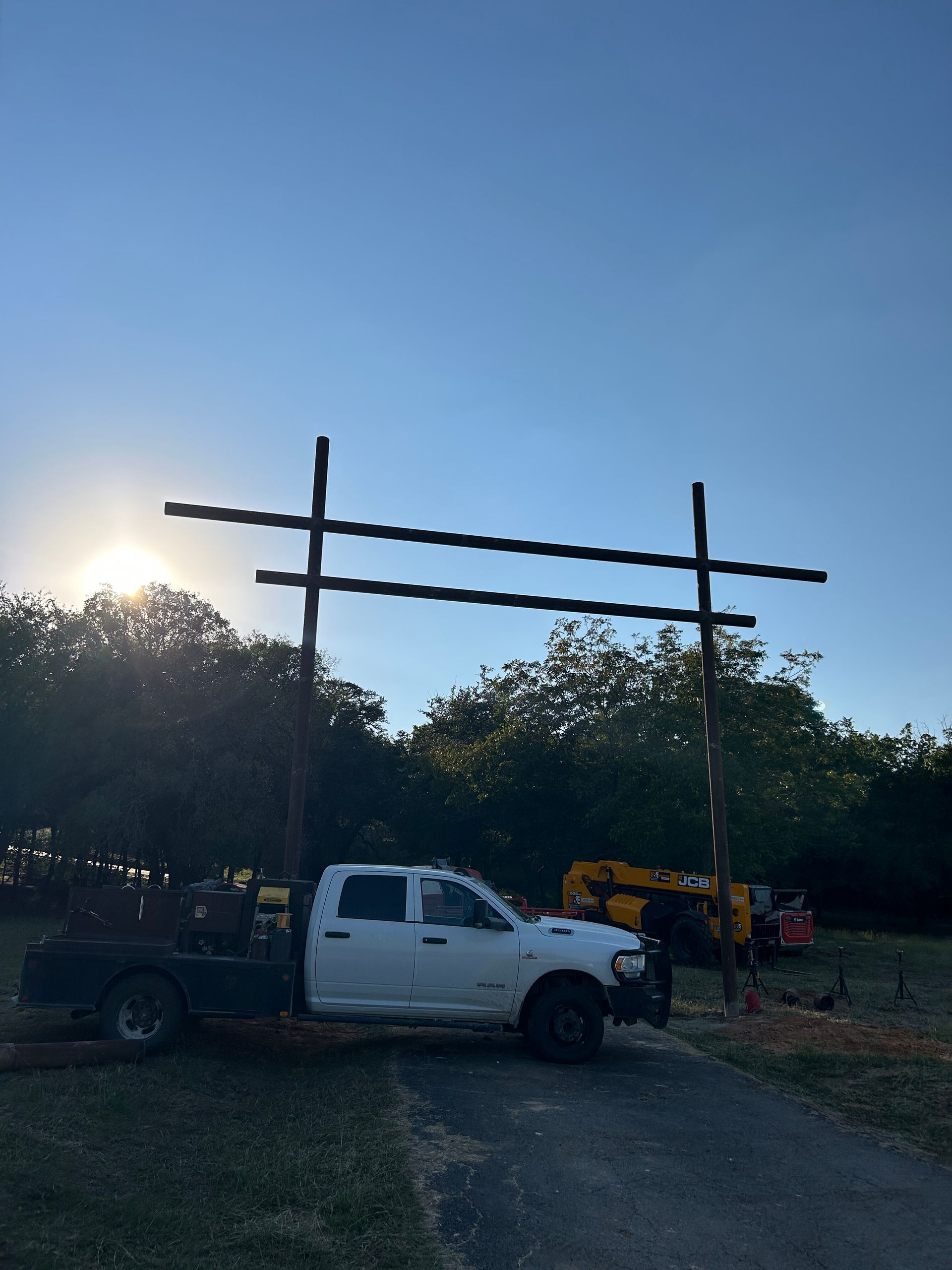 Pickup truck parked near a wooden frame at sunset with trees and construction equipment in the background