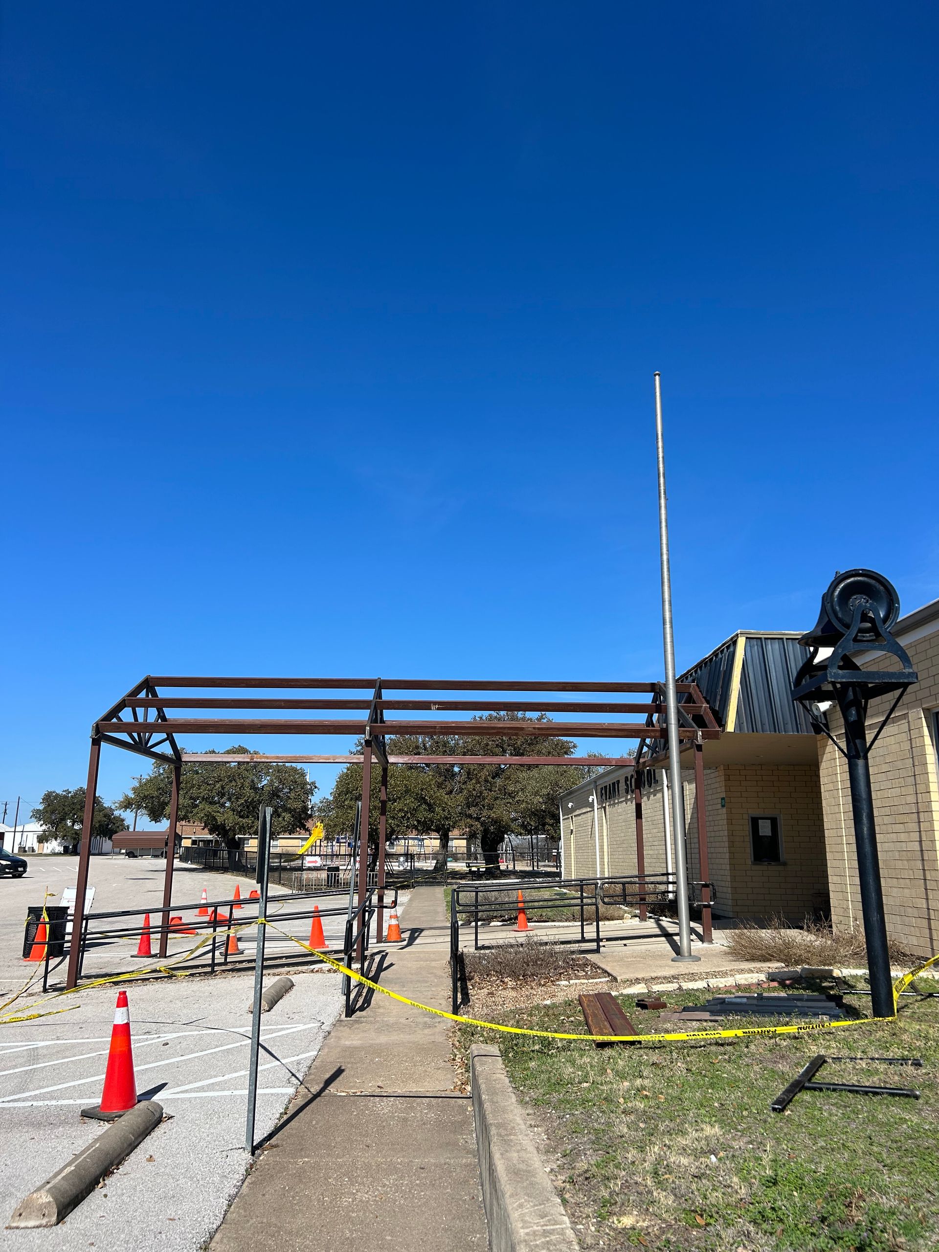 Construction site with steel frame, caution tape, orange cones, and a clear blue sky