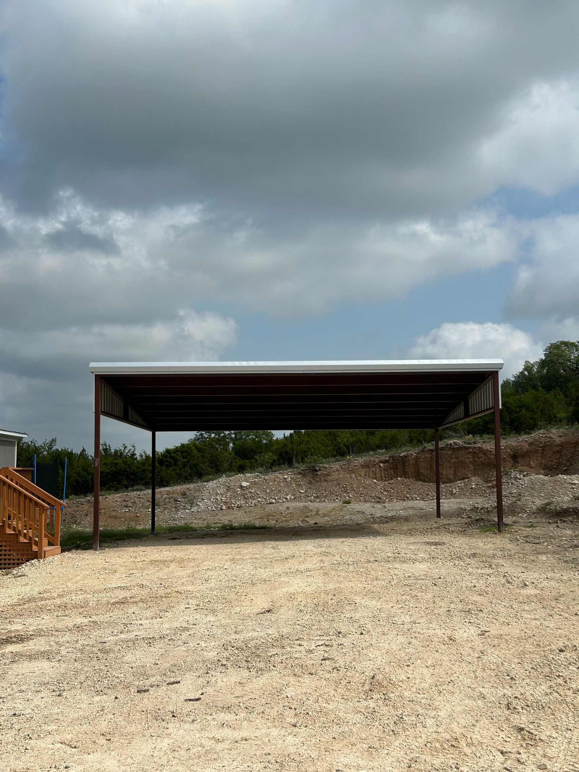 Open gravel lot with a metal-roofed shelter under a cloudy sky