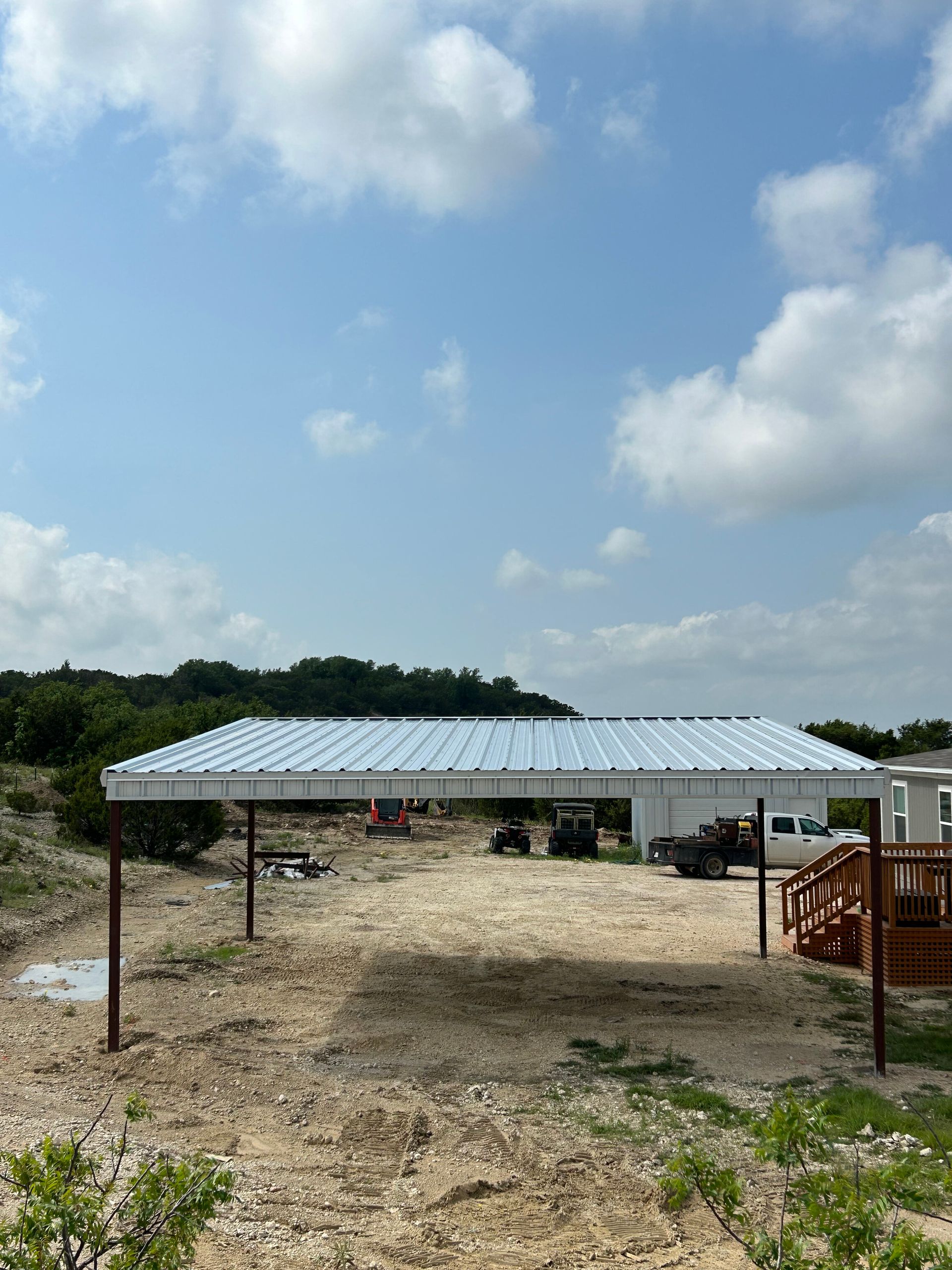 Open-air metal pavilion on a rocky dirt lot under a blue sky with clouds.