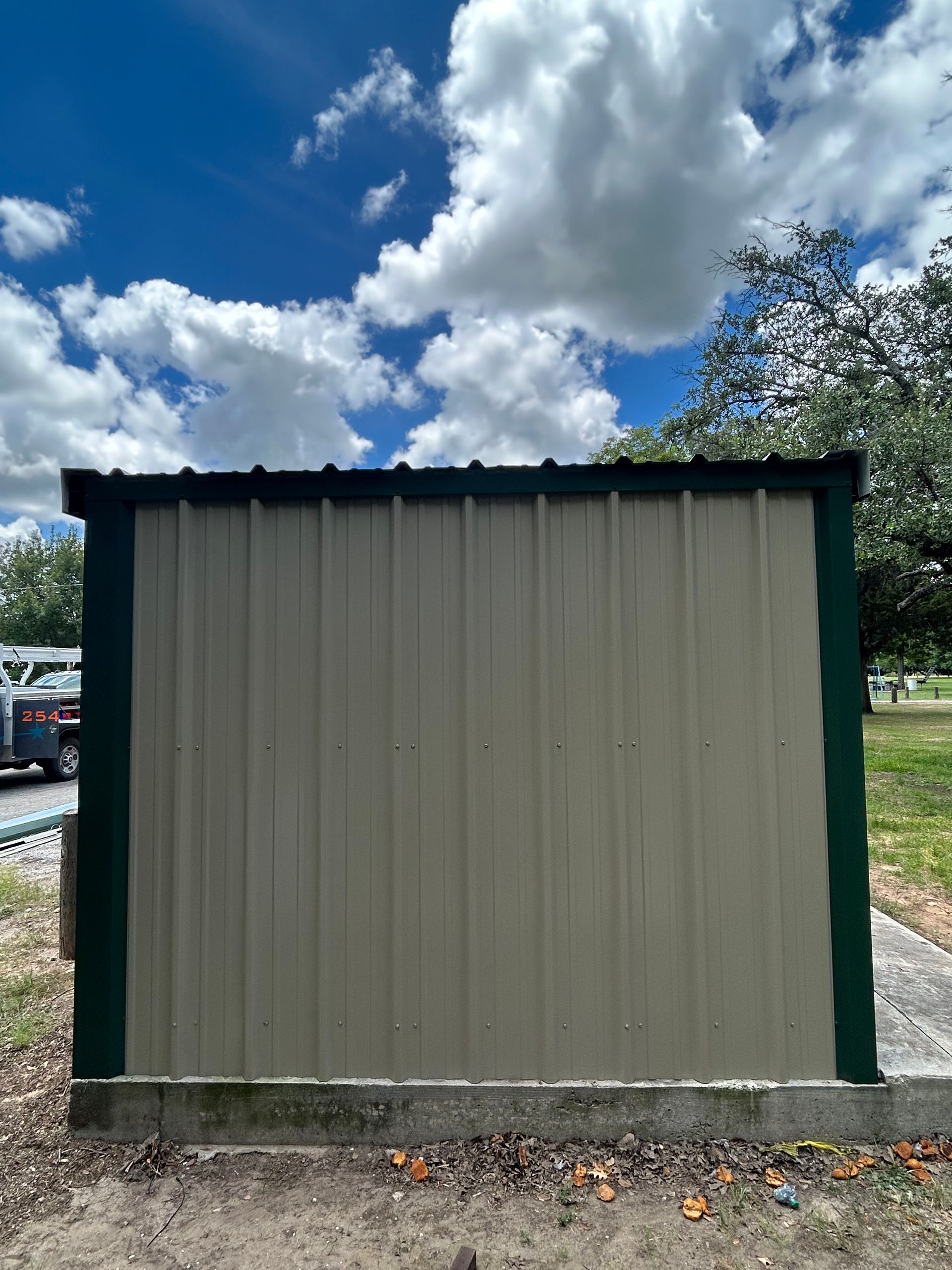 Small beige utility shed with green trim under a cloudy blue sky.