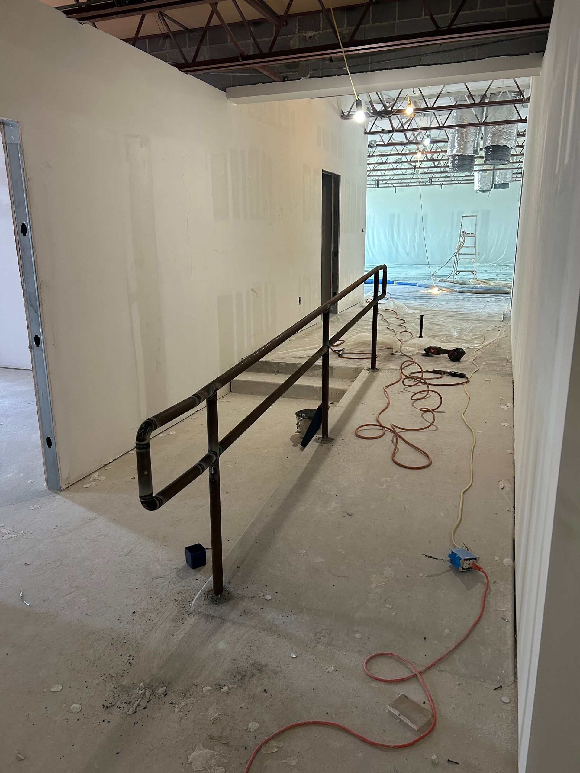 Construction hallway with black handrails, exposed ceiling, and scattered tools on the floor