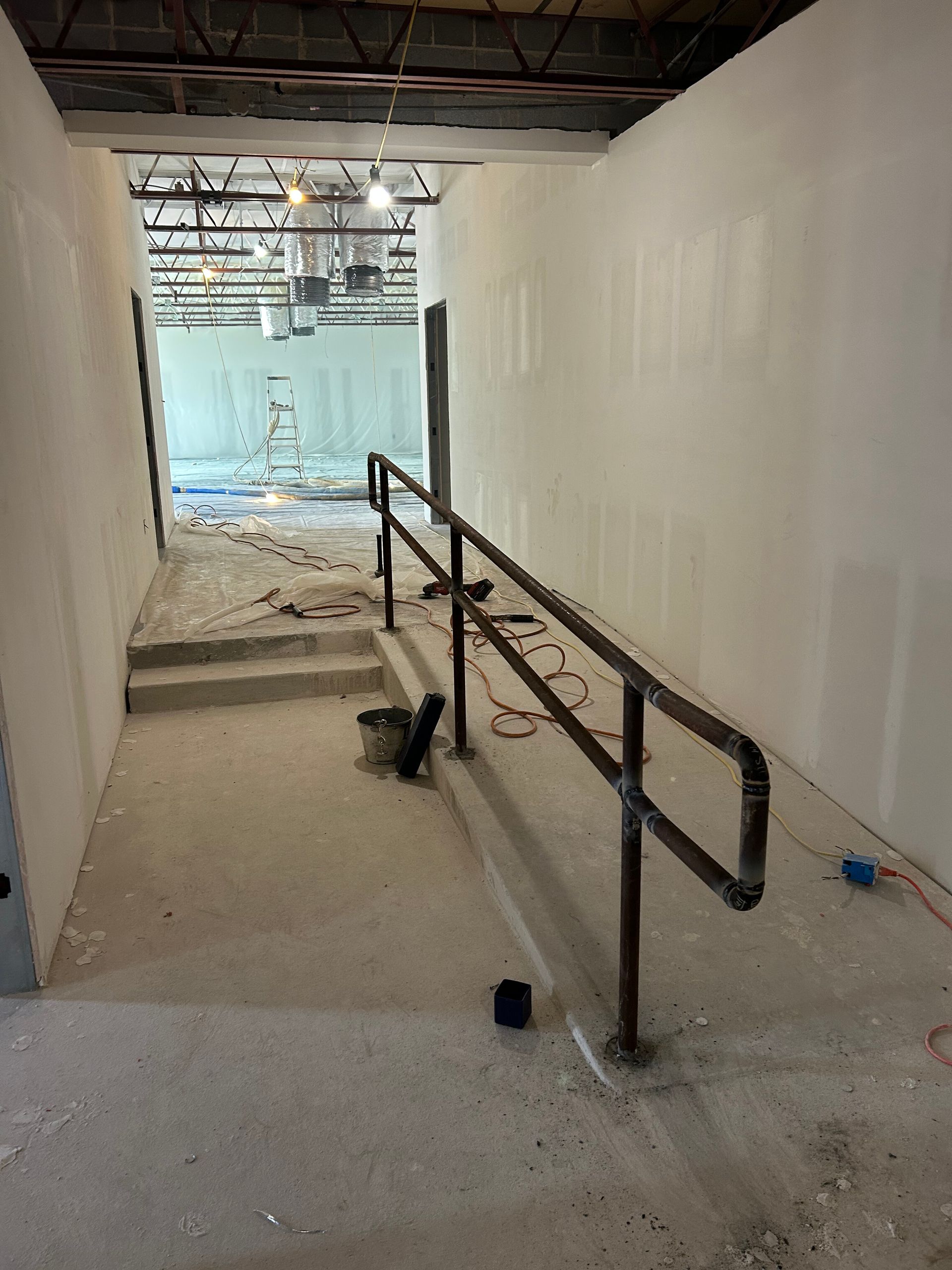 Indoor hallway under construction with a central metal handrail and debris on the floor