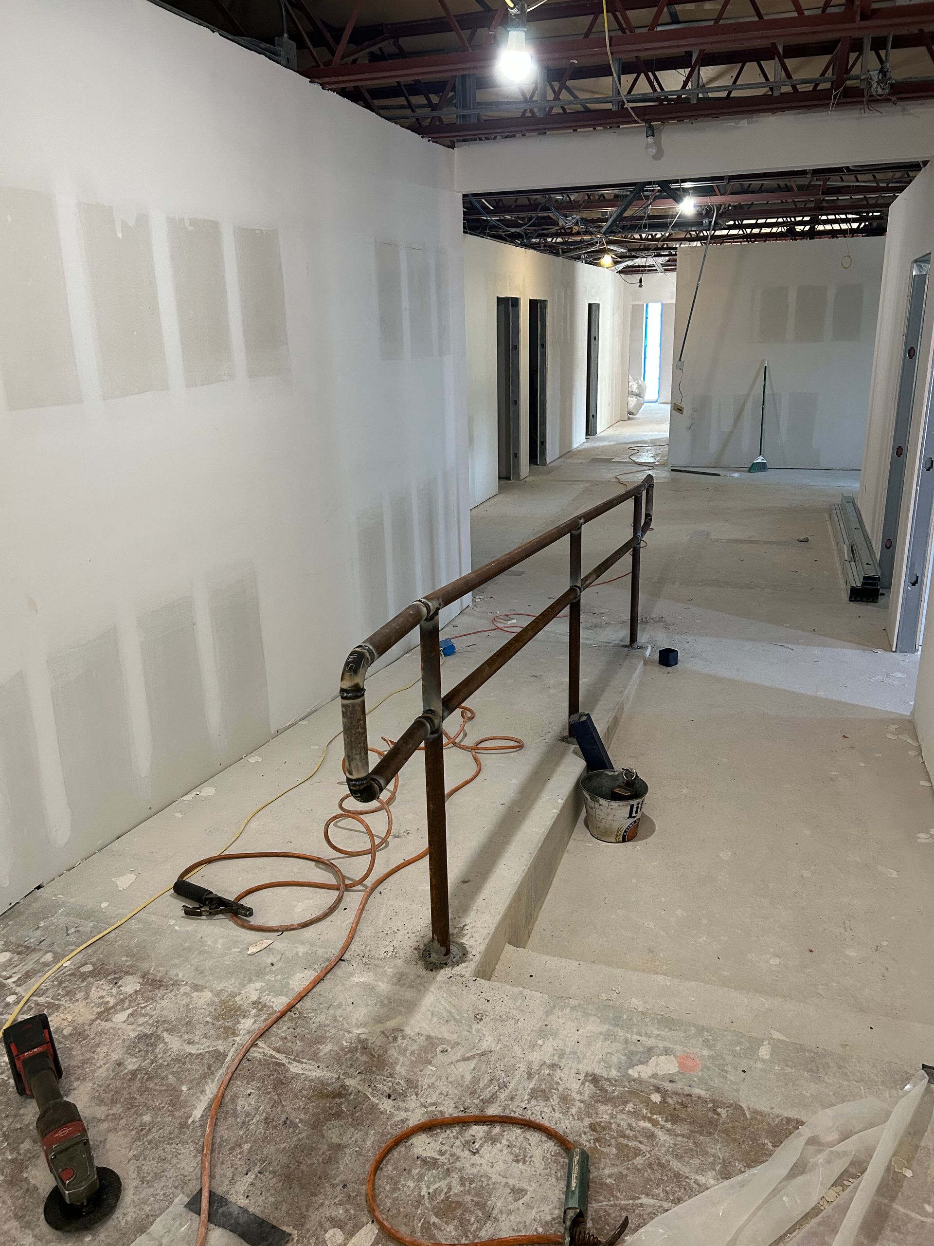 Narrow hallway under construction with drywall patches, scaffolding rails, cords, and debris on the floor
